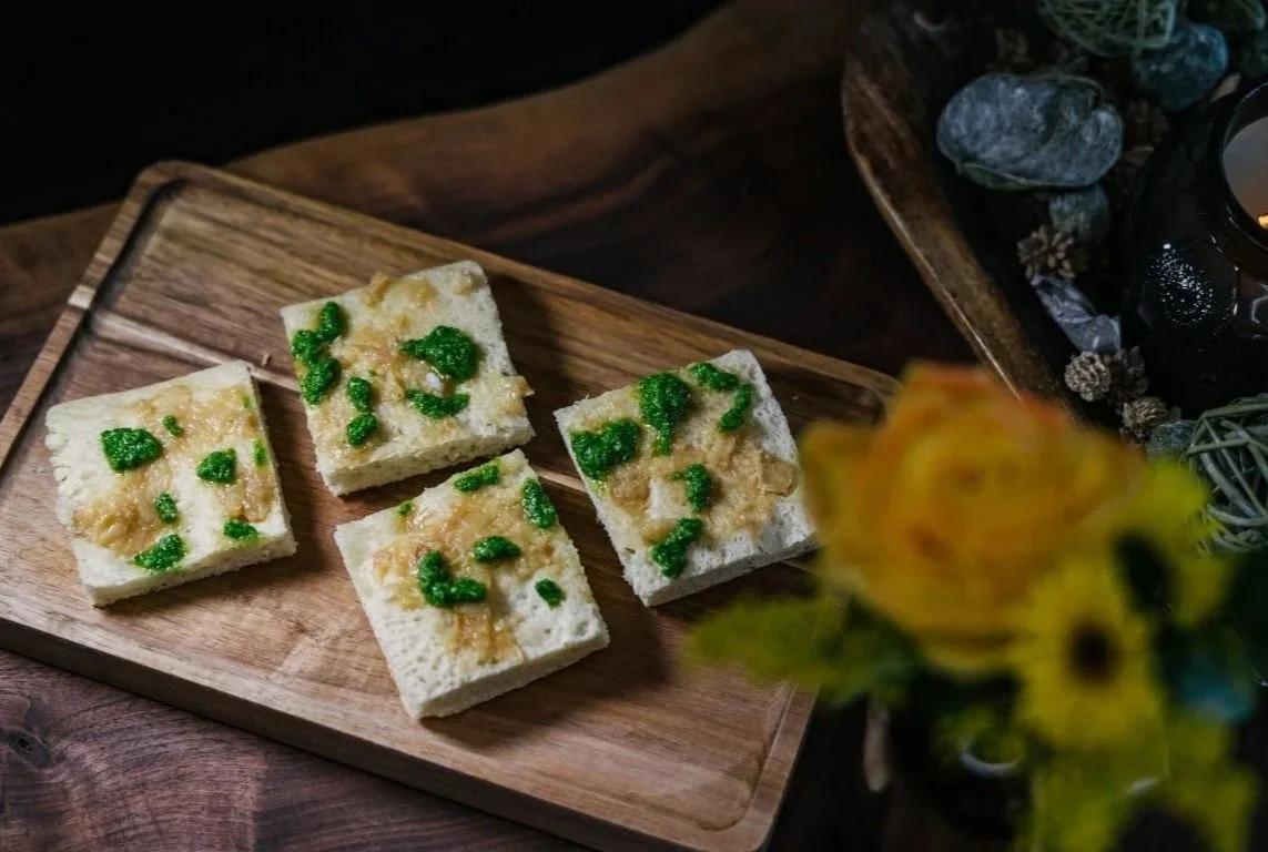 Four pieces of steamed bread with green and brown toppings on a wooden tray.