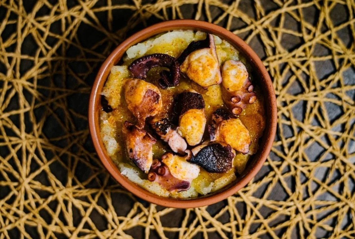 A bowl of cooked octopus with a yellow sauce, sitting on a woven rattan surface.
