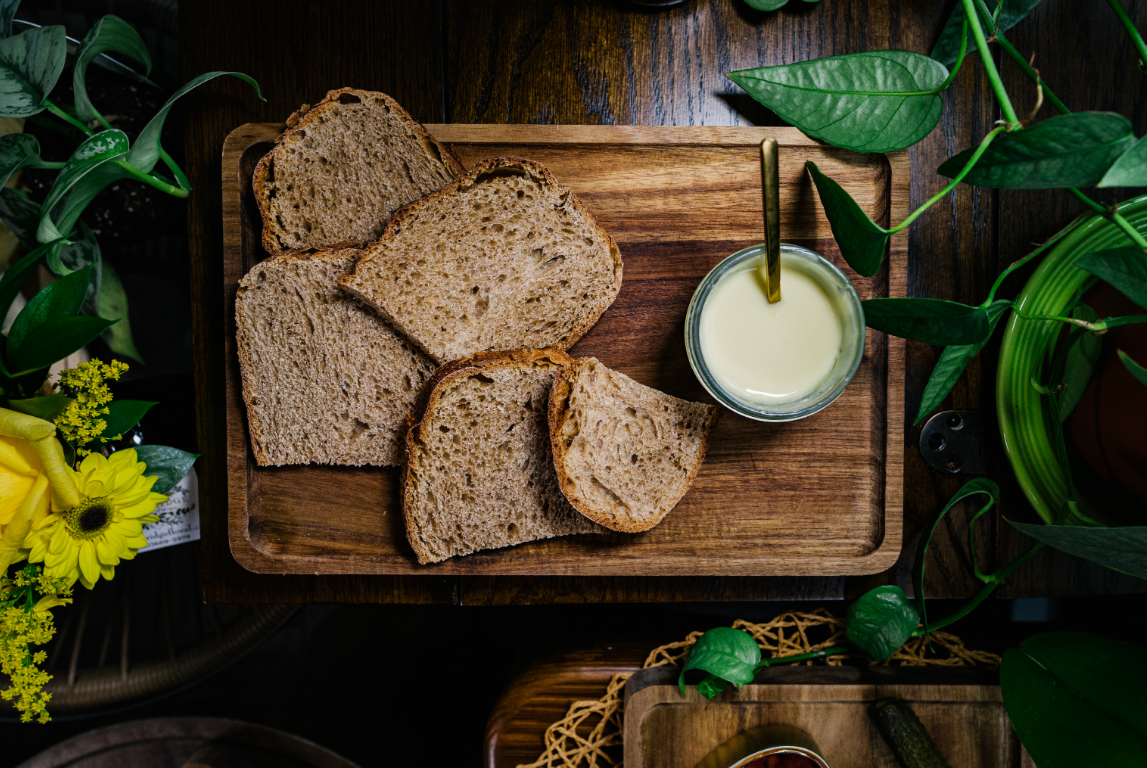Sliced bread and a glass of truffle infused brie on a wooden serving board, surrounded by green plants and yellow flowers. Spanish tapas.