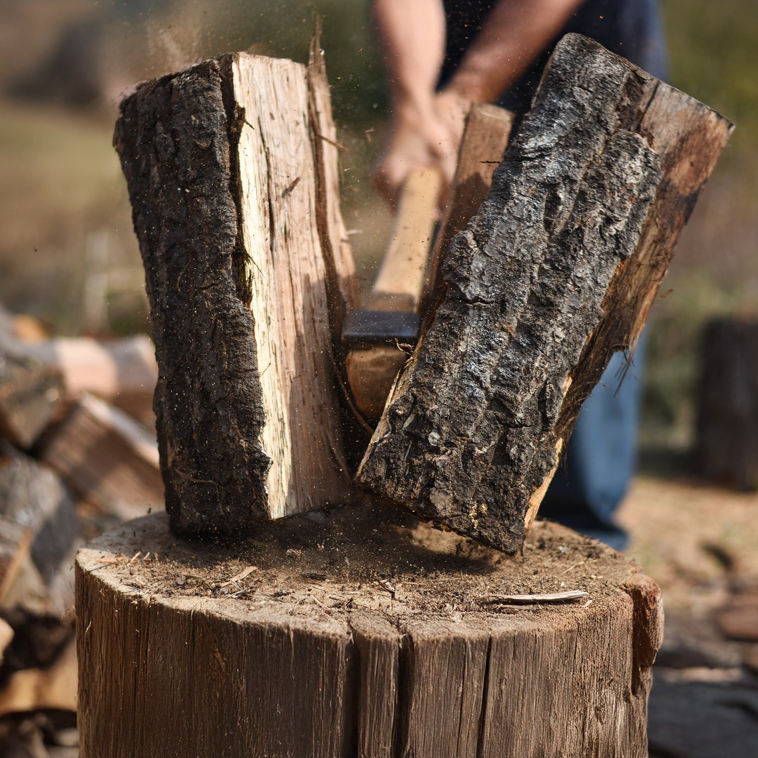 Someone chopping a large piece of wood with an axe, with wood chips flying in the air.