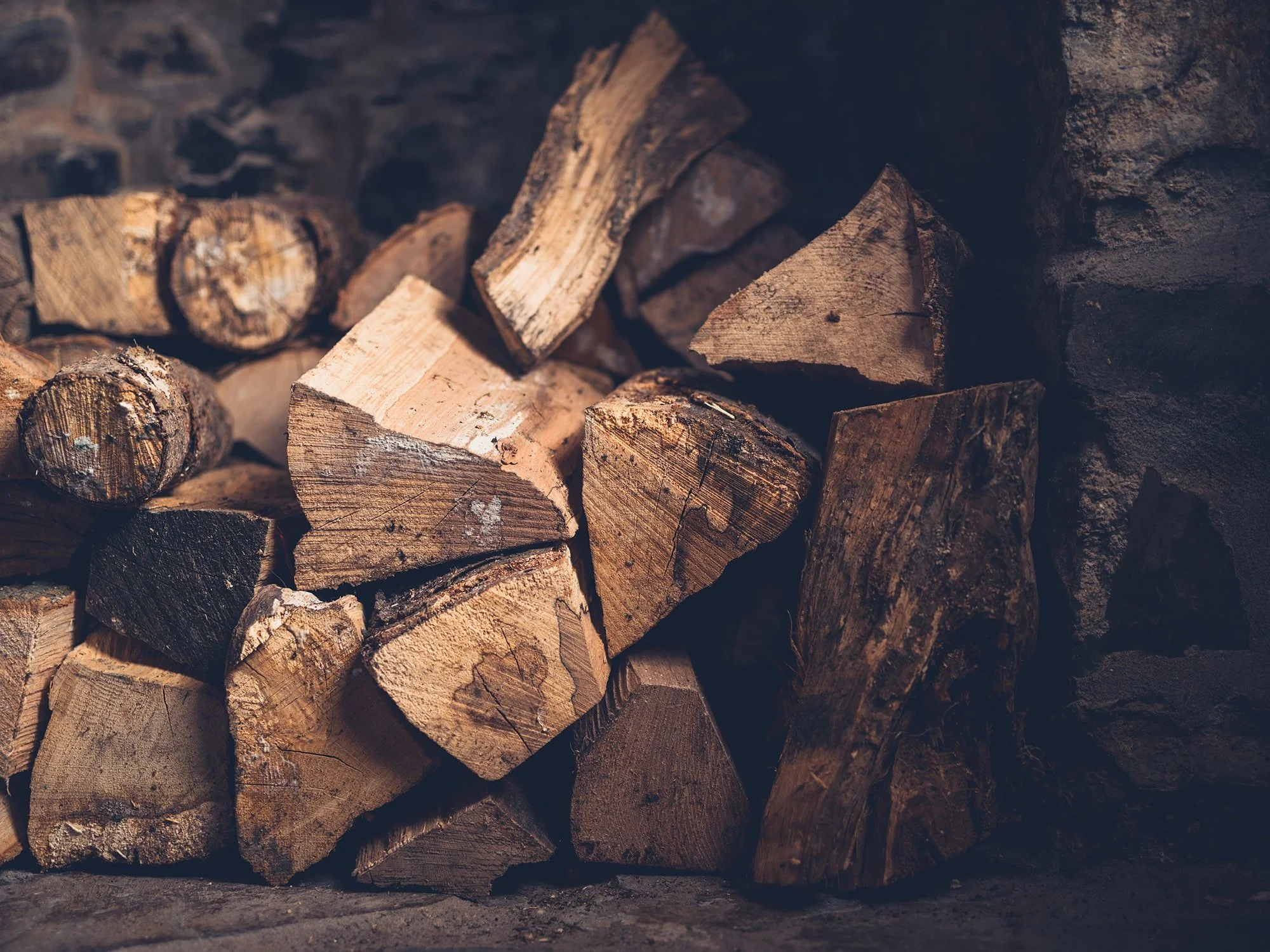 Stacked firewood against a stone wall.