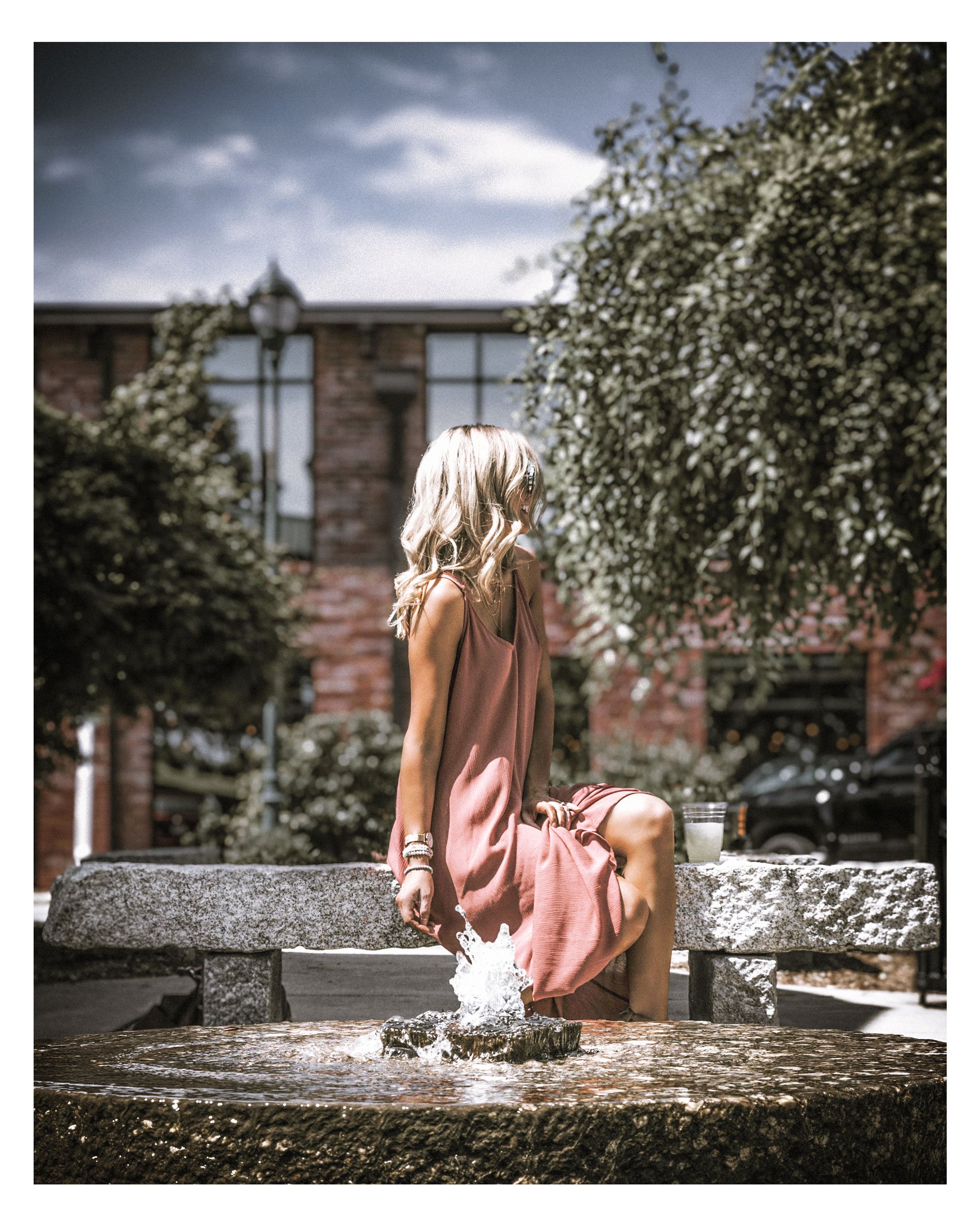 woman sitting behind a fountain with a coffee and sundress