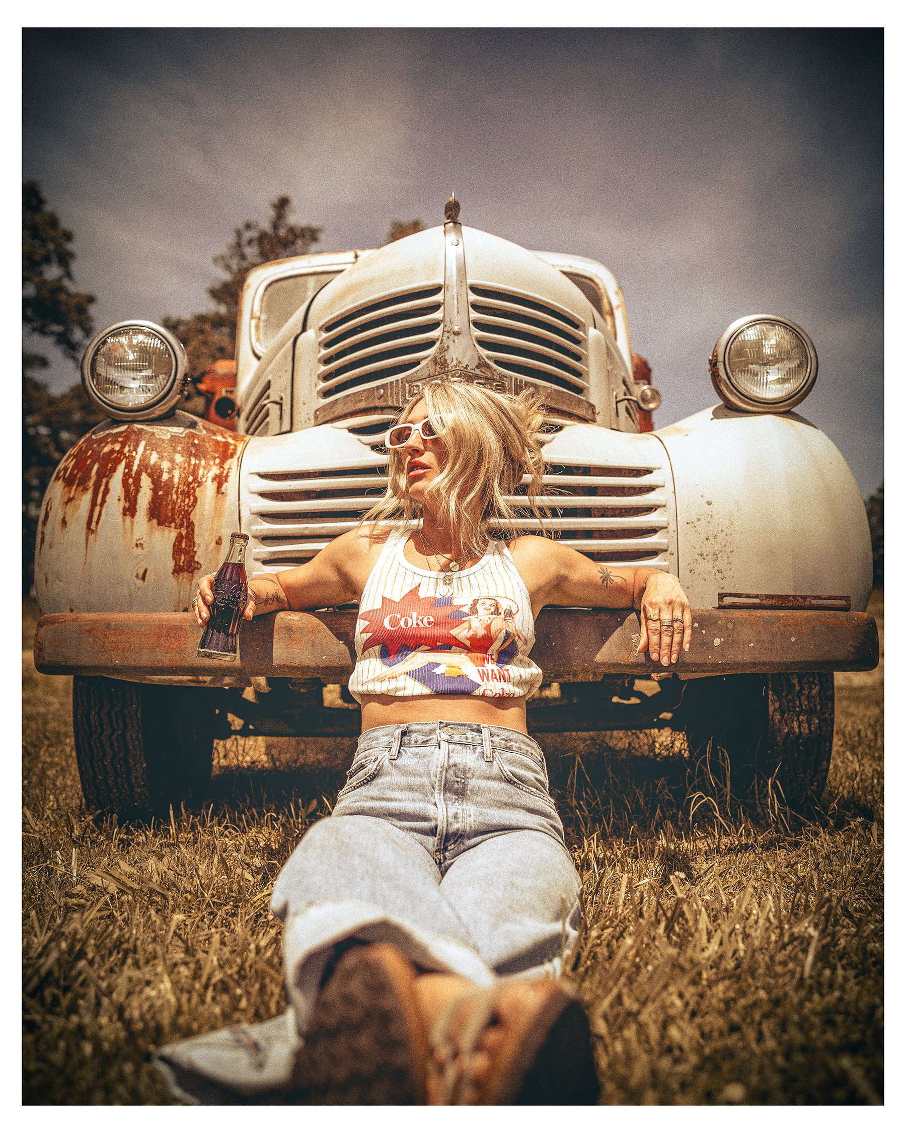 nostalgic photo of woman leaving against old car drinking a coke out of a glass bottle