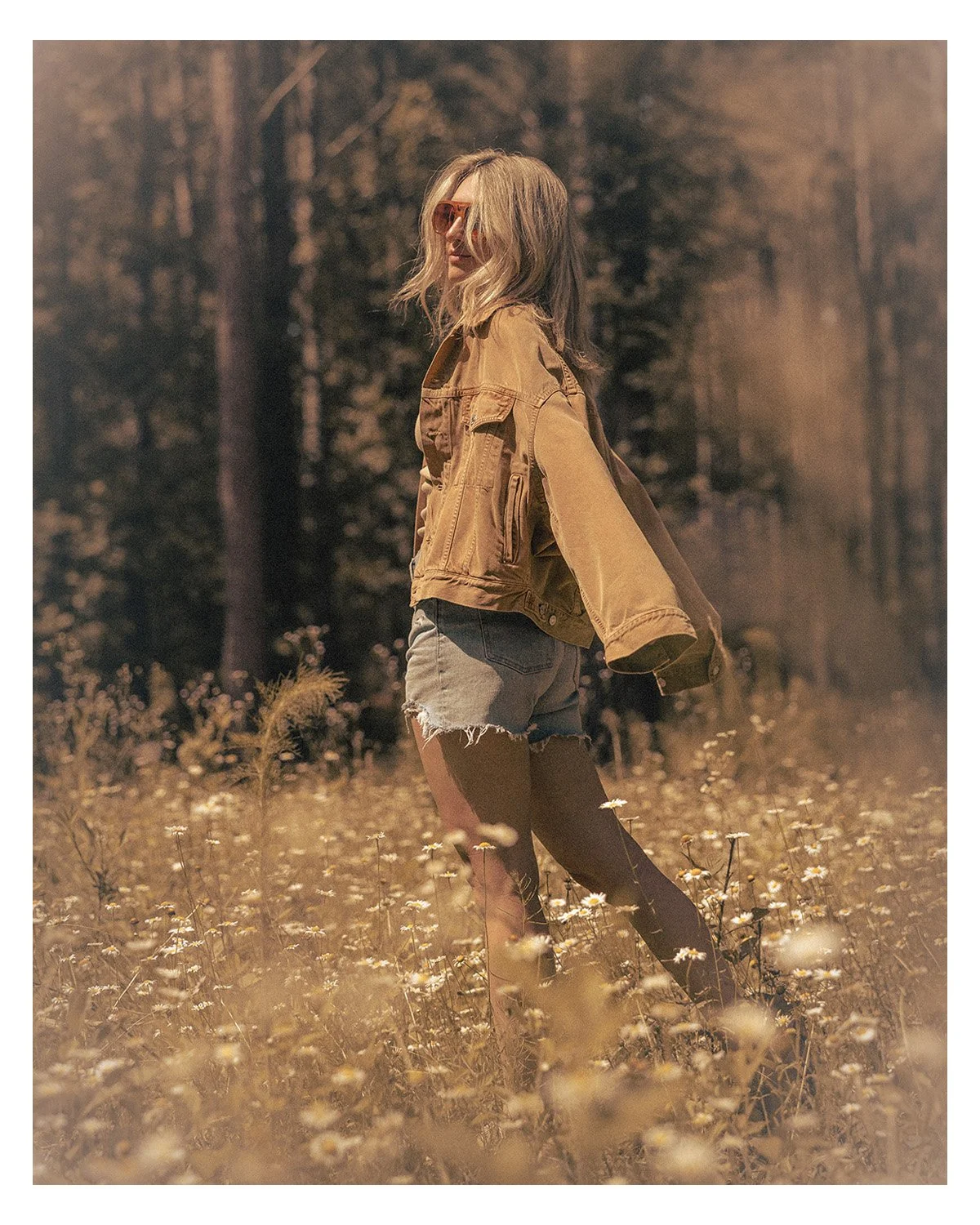 woman in denim jacket walking through a field of daisies