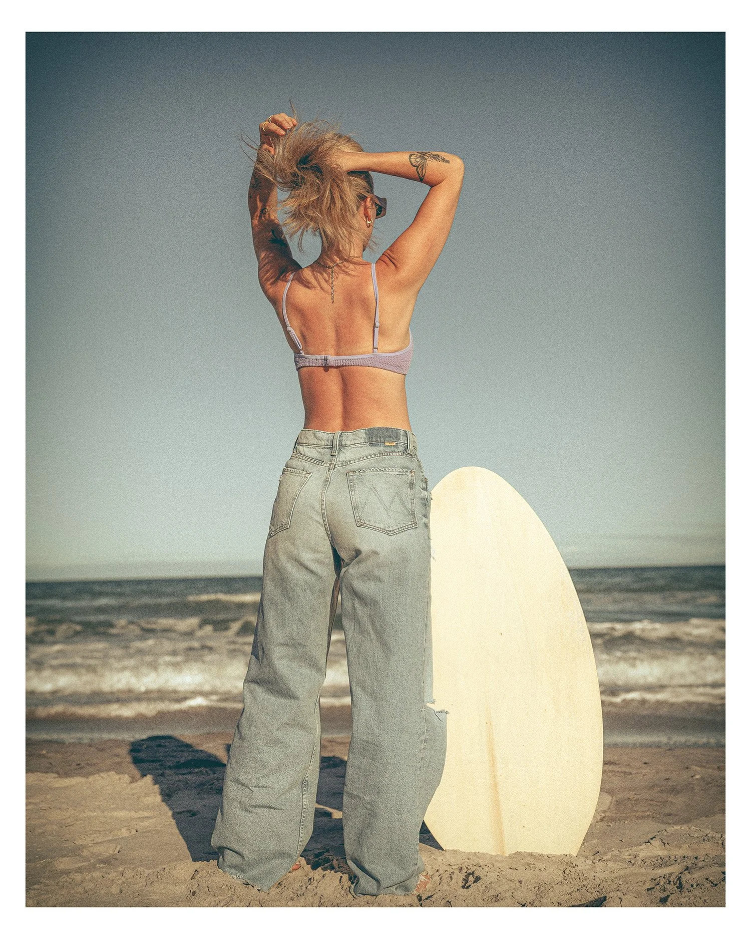 surfer skim boarding woman with bikini top looking out at the ocean
