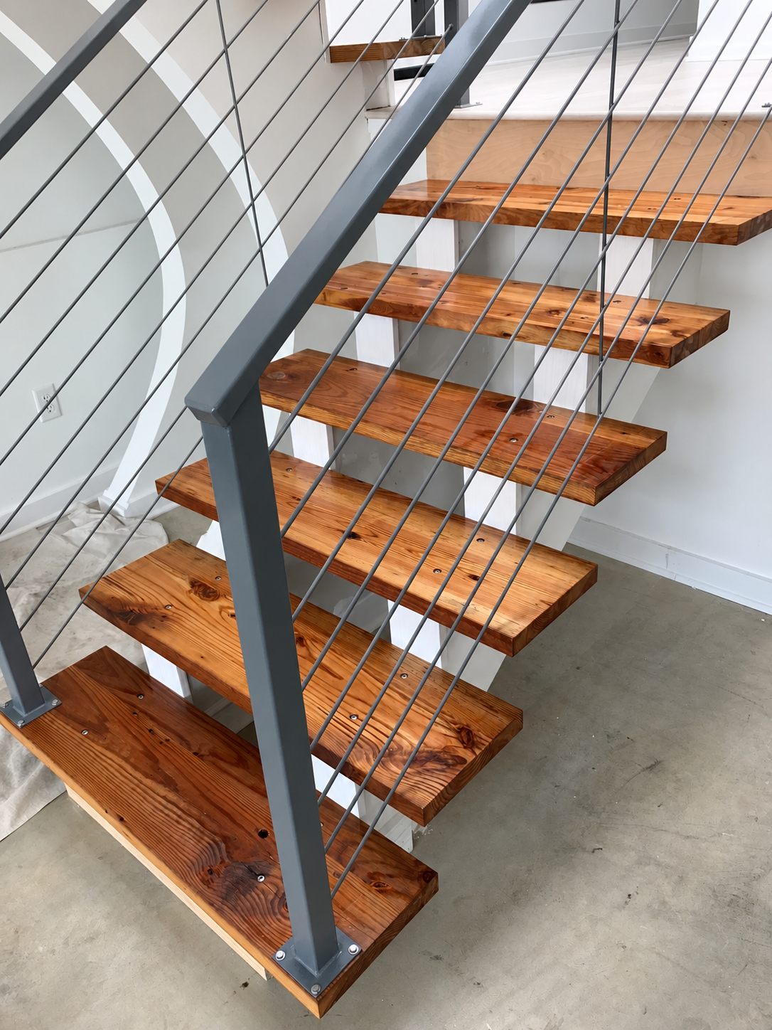 Wooden staircase with metal railing and cables in a modern interior.
