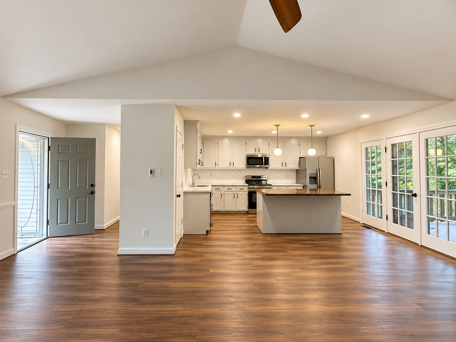 Open-concept kitchen with white cabinets, stainless steel appliances, wooden island, hardwood floors, and large glass French doors leading outside.
