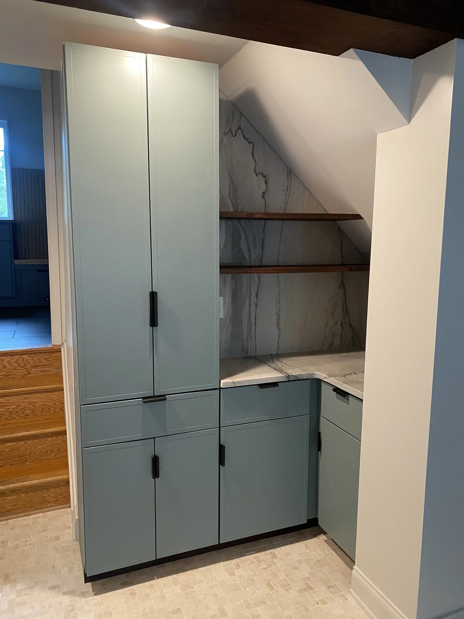 A modern kitchen cabinet unit with closed cupboards, featuring a two-tone design with light blue upper and lower cabinets separated by a light grey marble backsplash and wooden shelves.