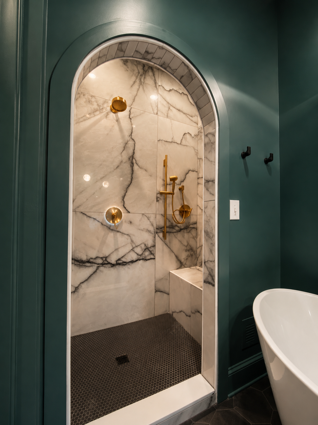 Marble walk-in shower with gold fixtures, green walls, and a partial view of a white bathtub.