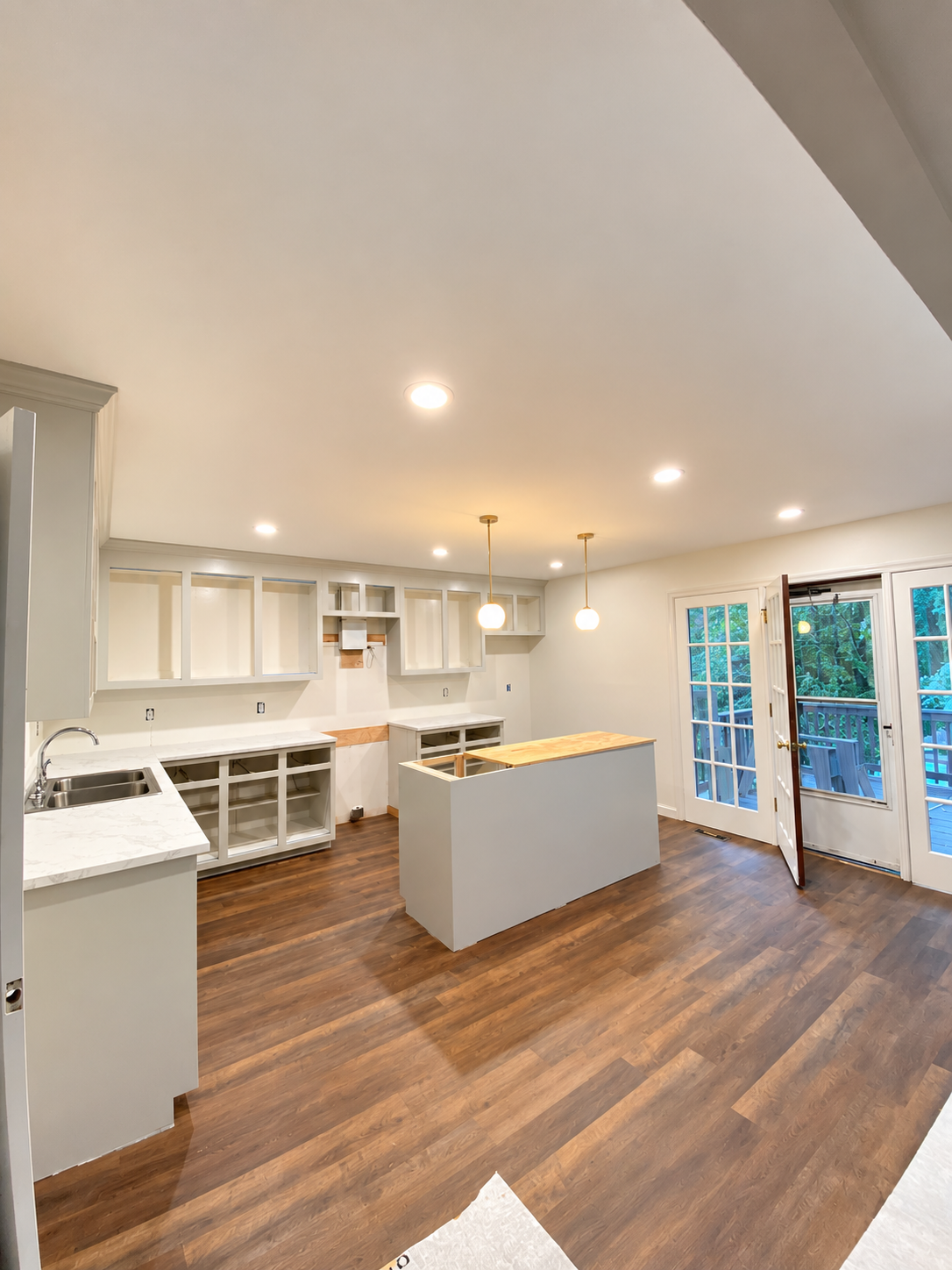 Empty kitchen with white cabinets, open shelves, a small kitchen island, hardwood floors, and a glass door leading to a balcony, during daytime.