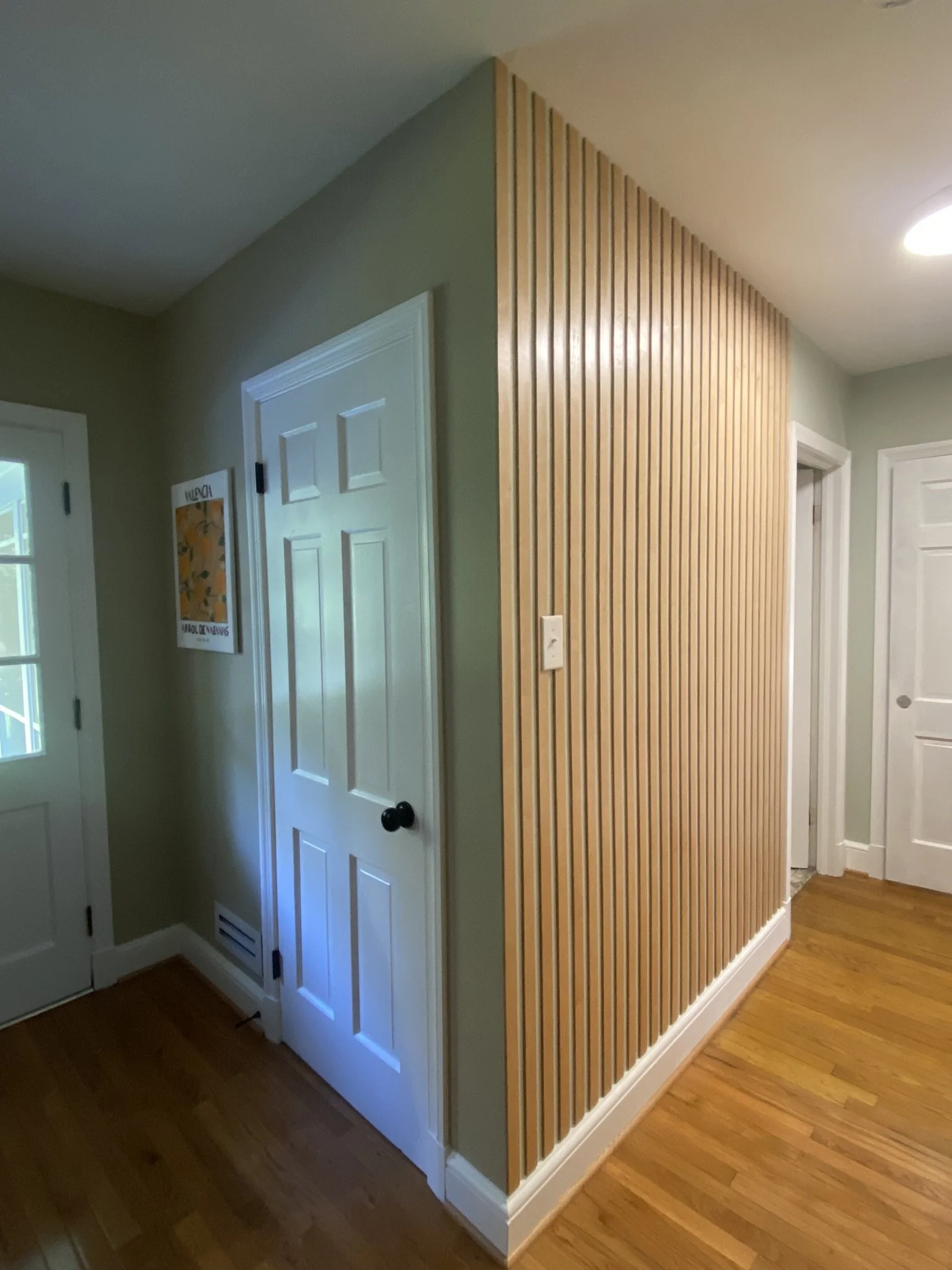 Interior hallway corner with a wooden slat accent wall, white doors, and light-colored walls with hardwood flooring.