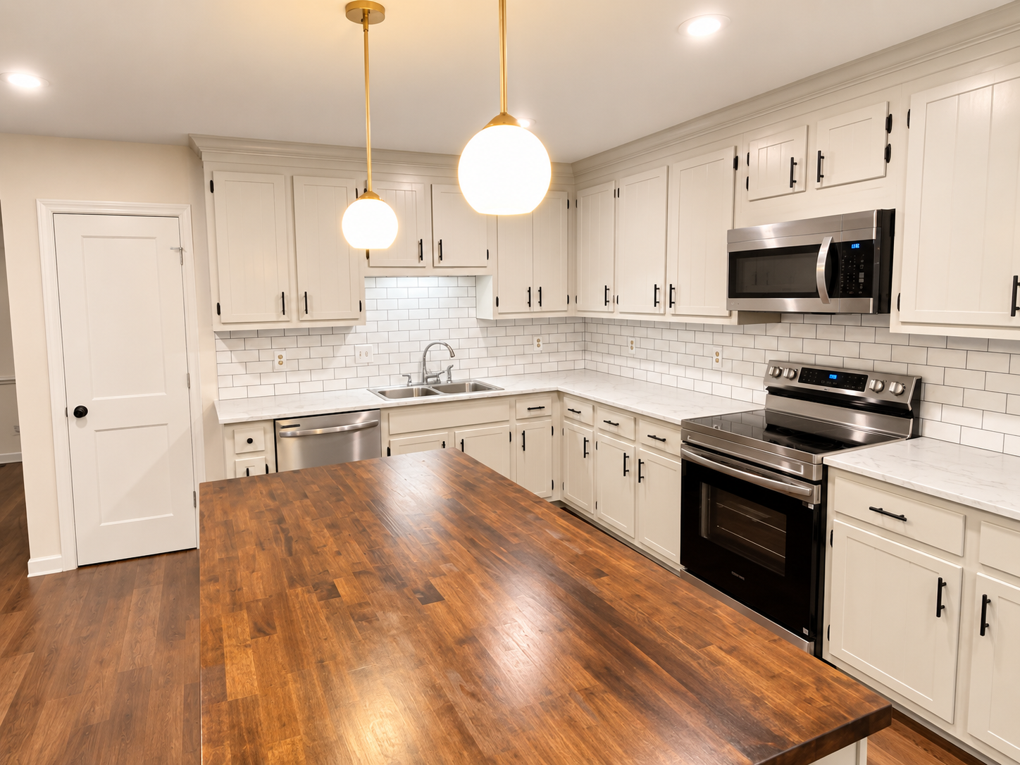 Modern white kitchen with wood island, stainless steel appliances, pendant lights, subway tile backsplash, and upper and lower cabinets.