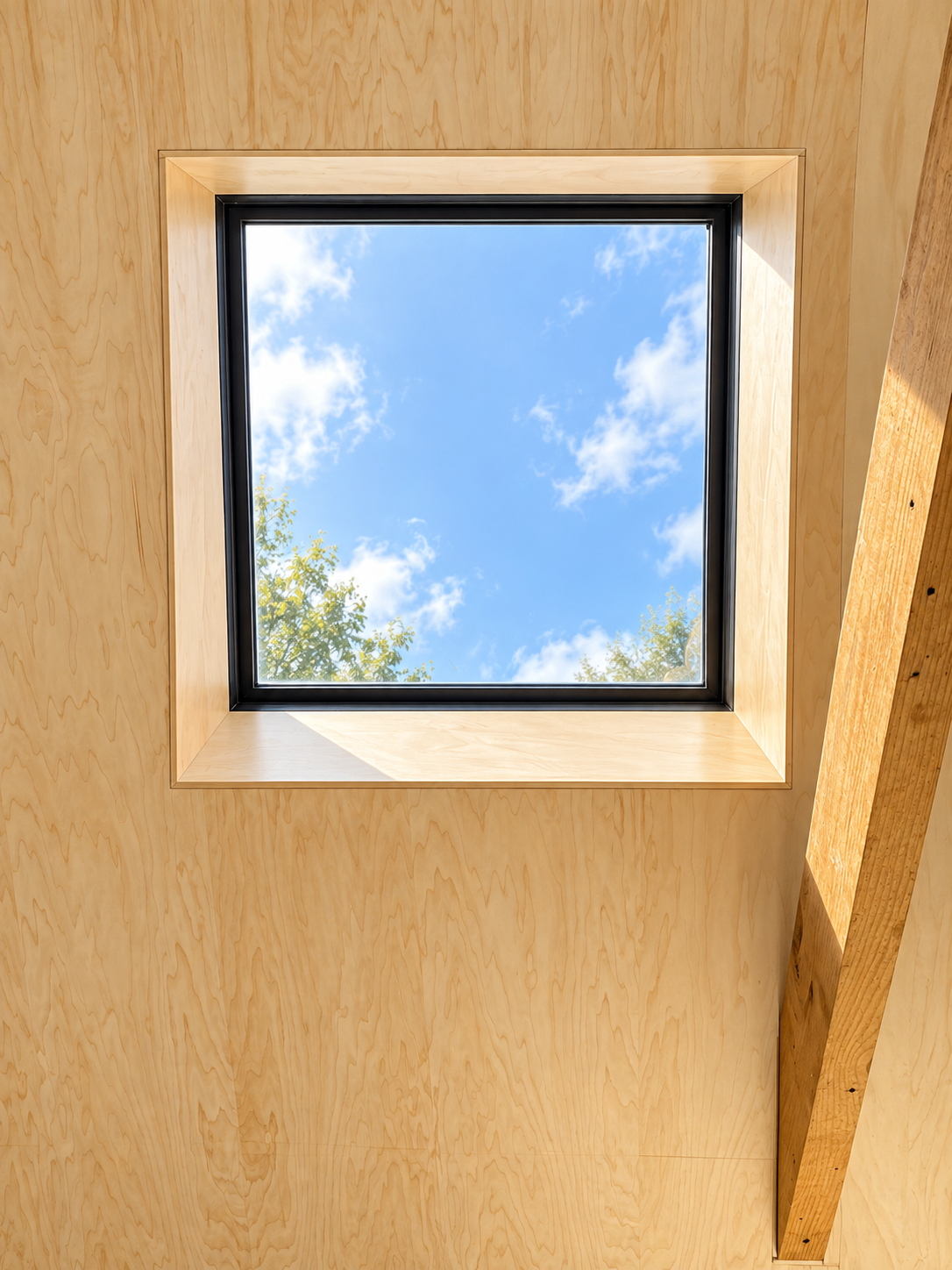 View of blue sky with clouds through a square skylight in a wooden ceiling.