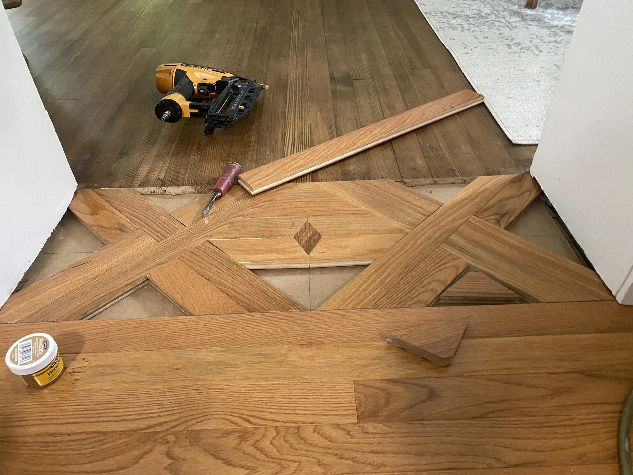 Wood flooring being installed with a nail gun and a cordless screwdriver on the floor.
