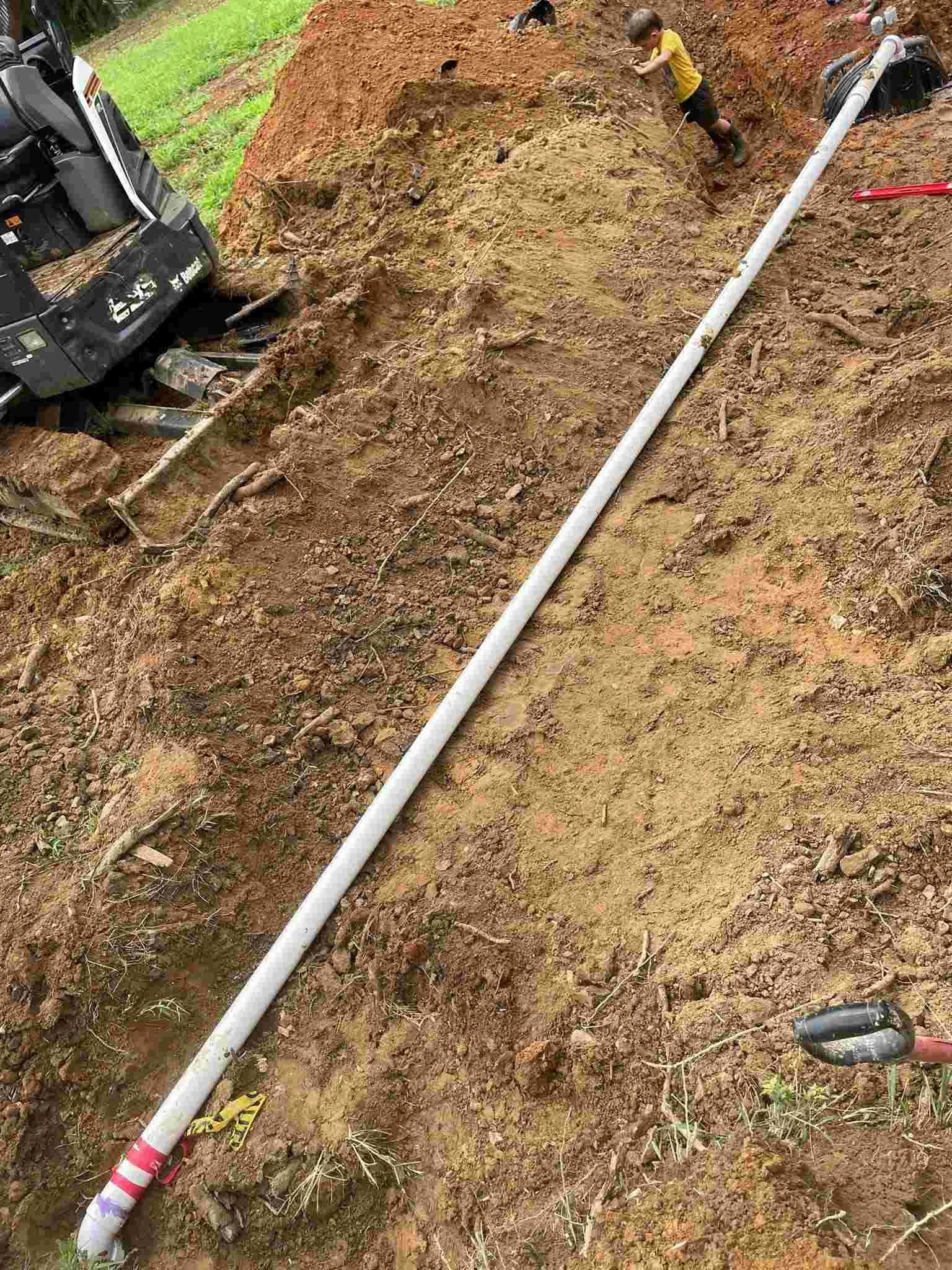 Sewer line installation on hillside with white PVC pipe and Bobcat excavator in Middle Tennesse