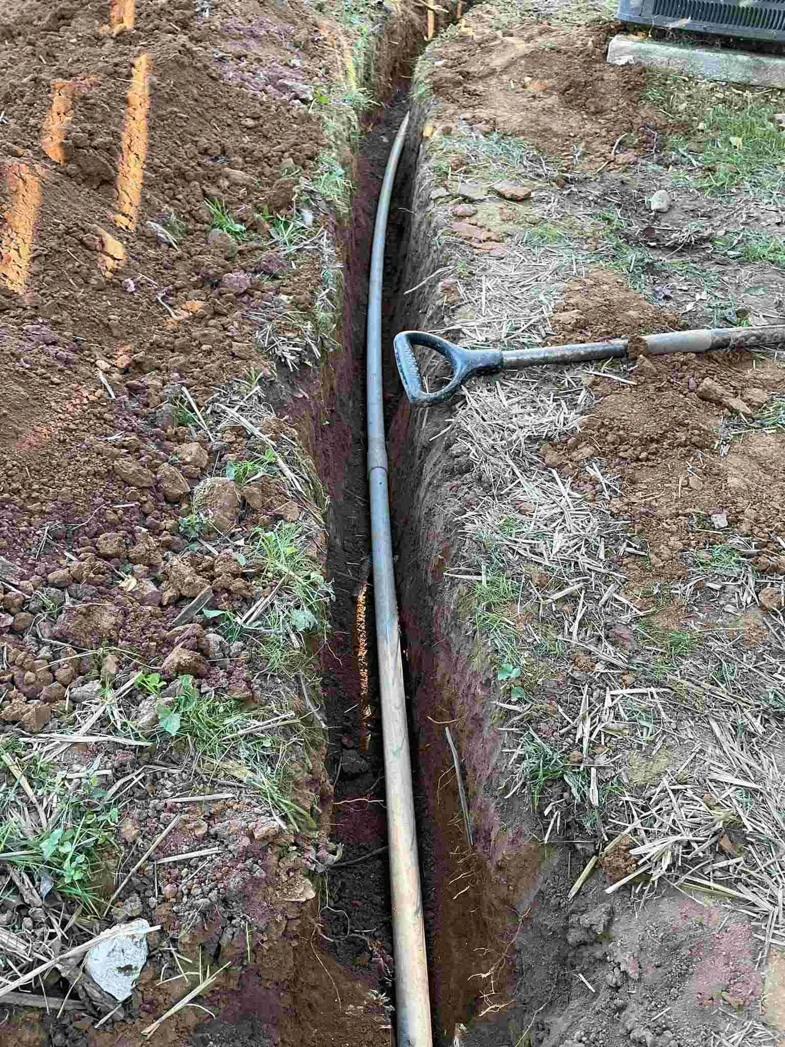 A trench with a pipe installed in the ground with a shovel resting on the edge.