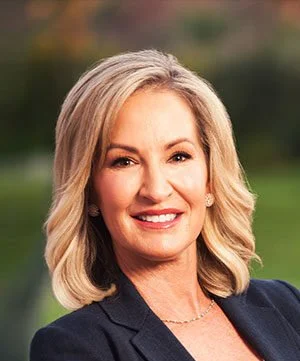Portrait of a smiling woman with blonde hair wearing a dark blazer outdoors.