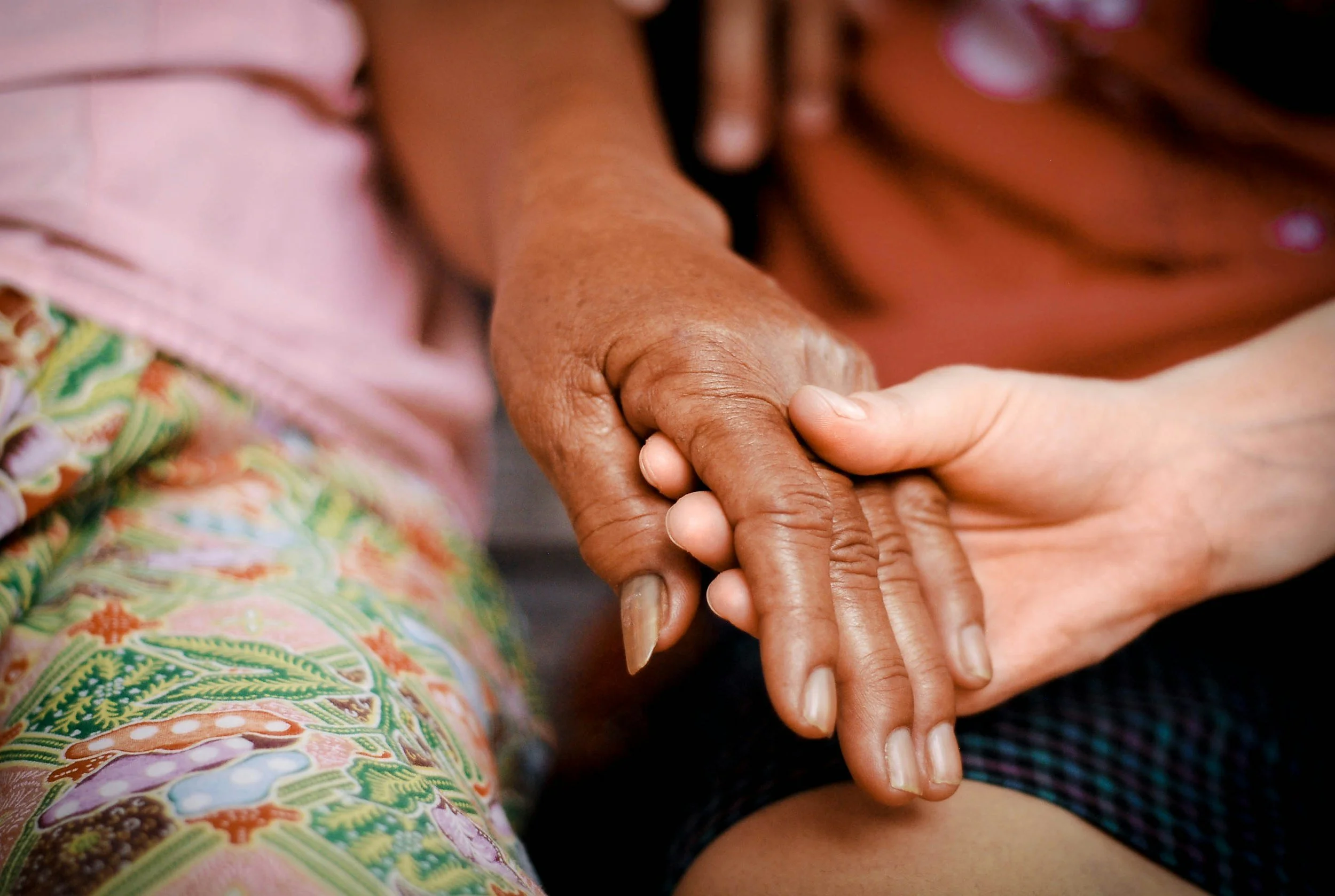 Close-up of two hands holding each other, one appears older with darker skin and the other younger with lighter skin.