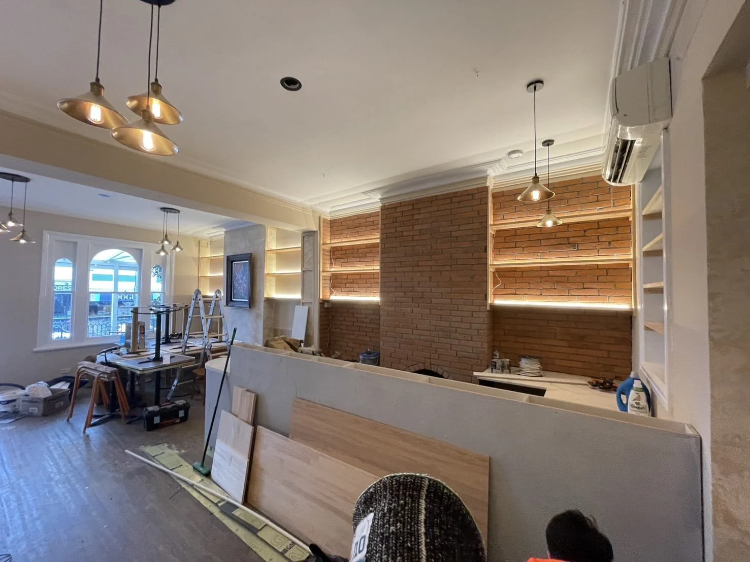 Interior of a room under renovation with exposed brick walls, open shelves, construction materials, and furniture.