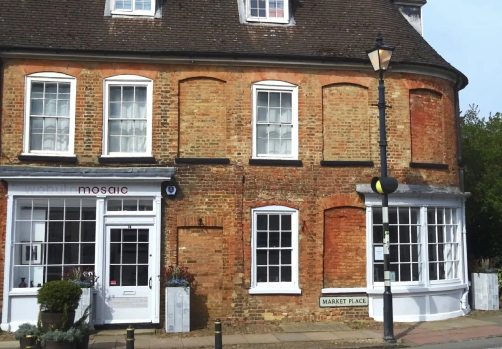 Brick building with white-framed windows and a storefront named Mosaic, located on Market Place, with a lamp post in front.
