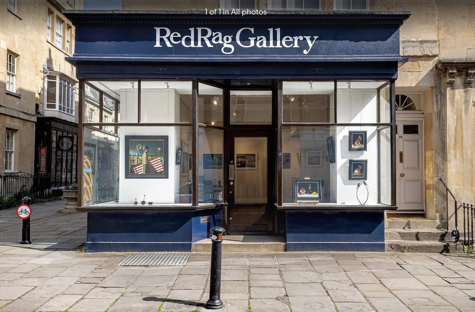 The storefront of the Red Rag Gallery with large glass windows displaying artwork inside and the sculptures by Jonathan Hateley, a dark blue exterior, and an entrance in the centre with steps leading up to it.