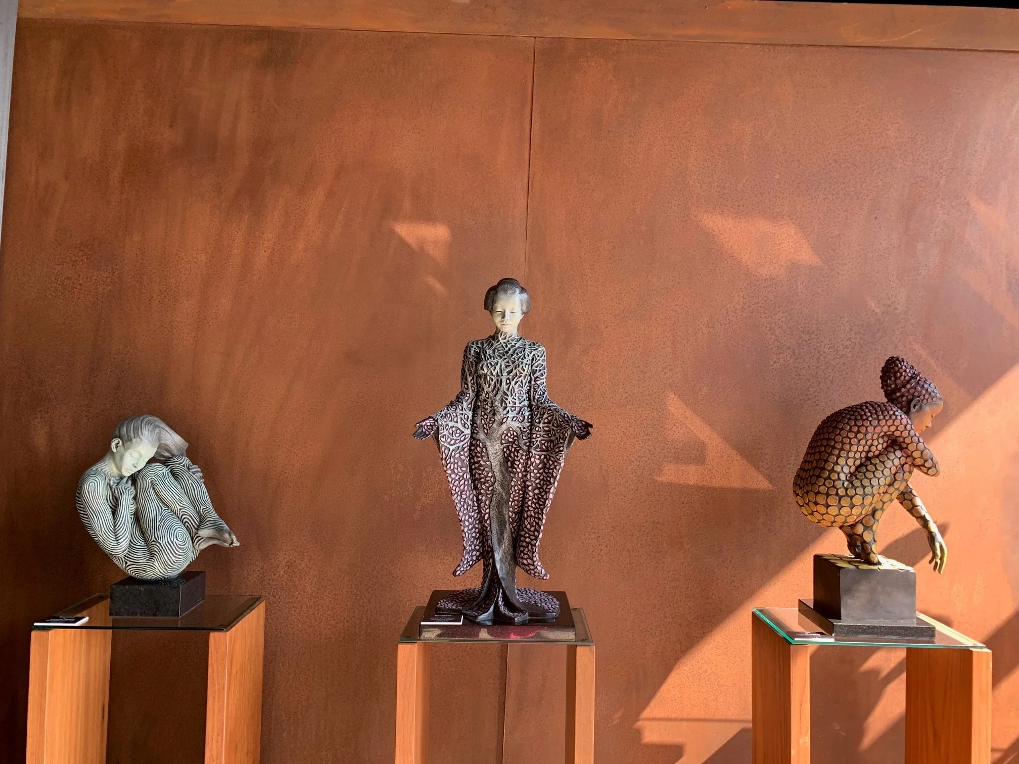 Three artistic sculptures, by Jonathan Hateley, of women, stylised with intricate details in their clothing and hair.