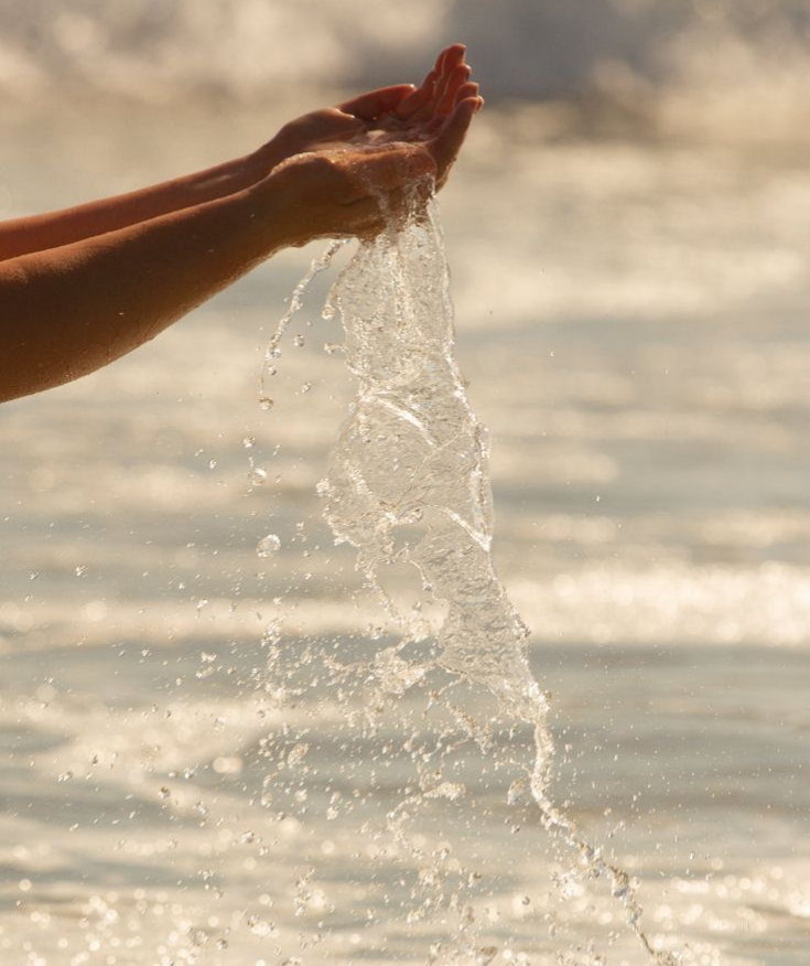 Hands splashing water in a body of water during sunset