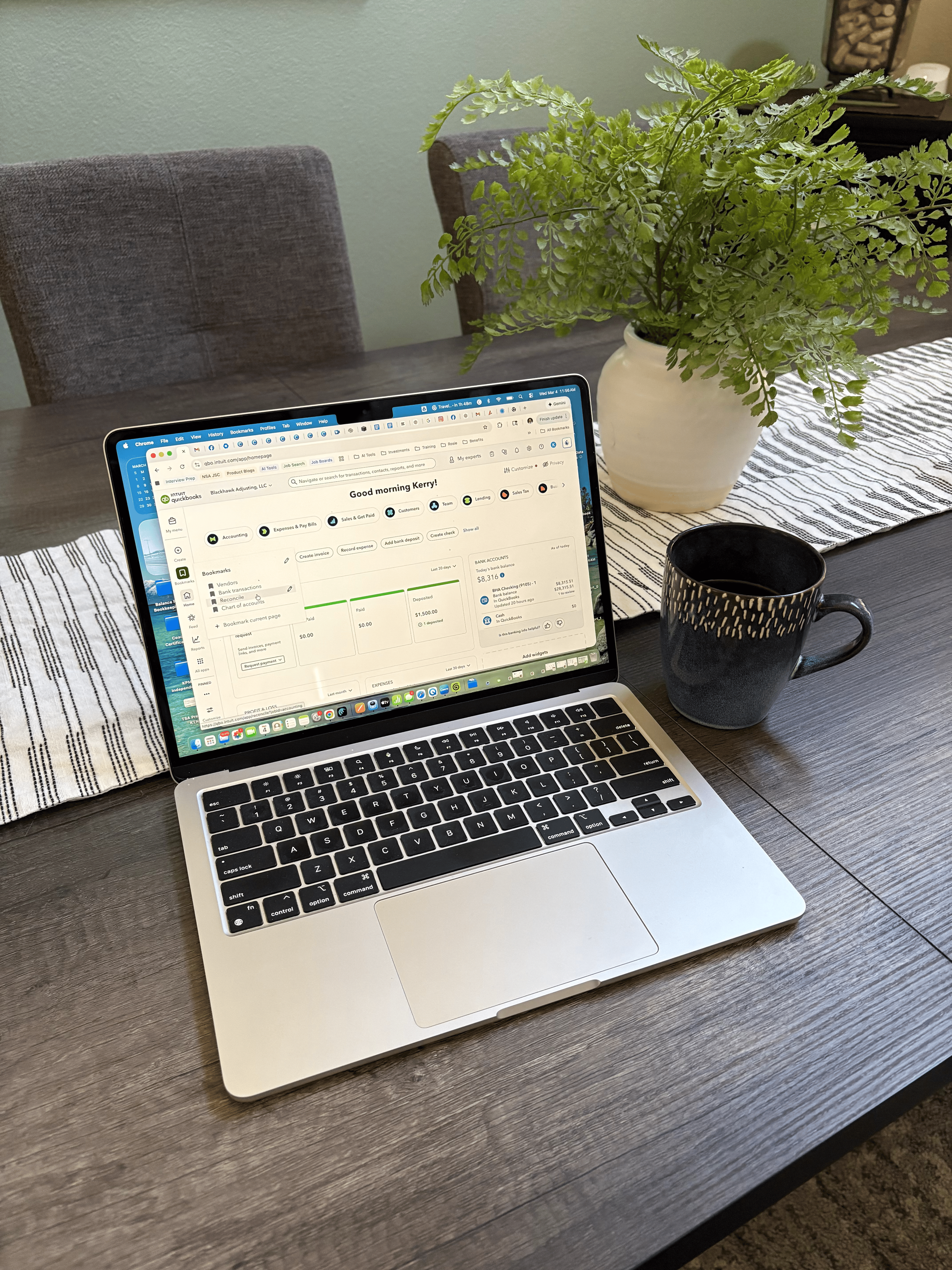 Laptop in working mode open on a table with a plant and cup of coffee beside it.