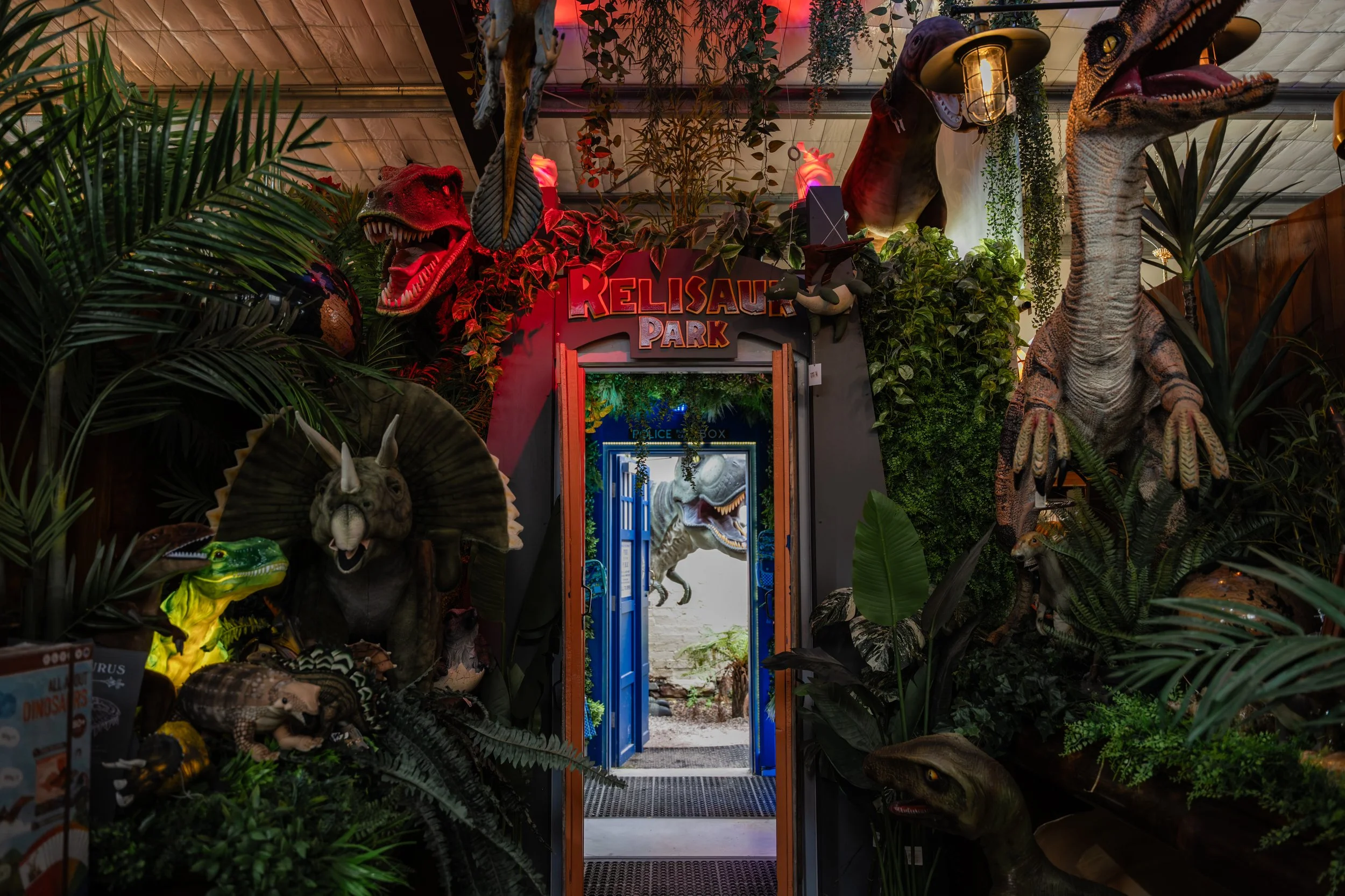Entrance to Relisaur Park with dinosaur models surrounded by lush greenery and jungle-themed decor.