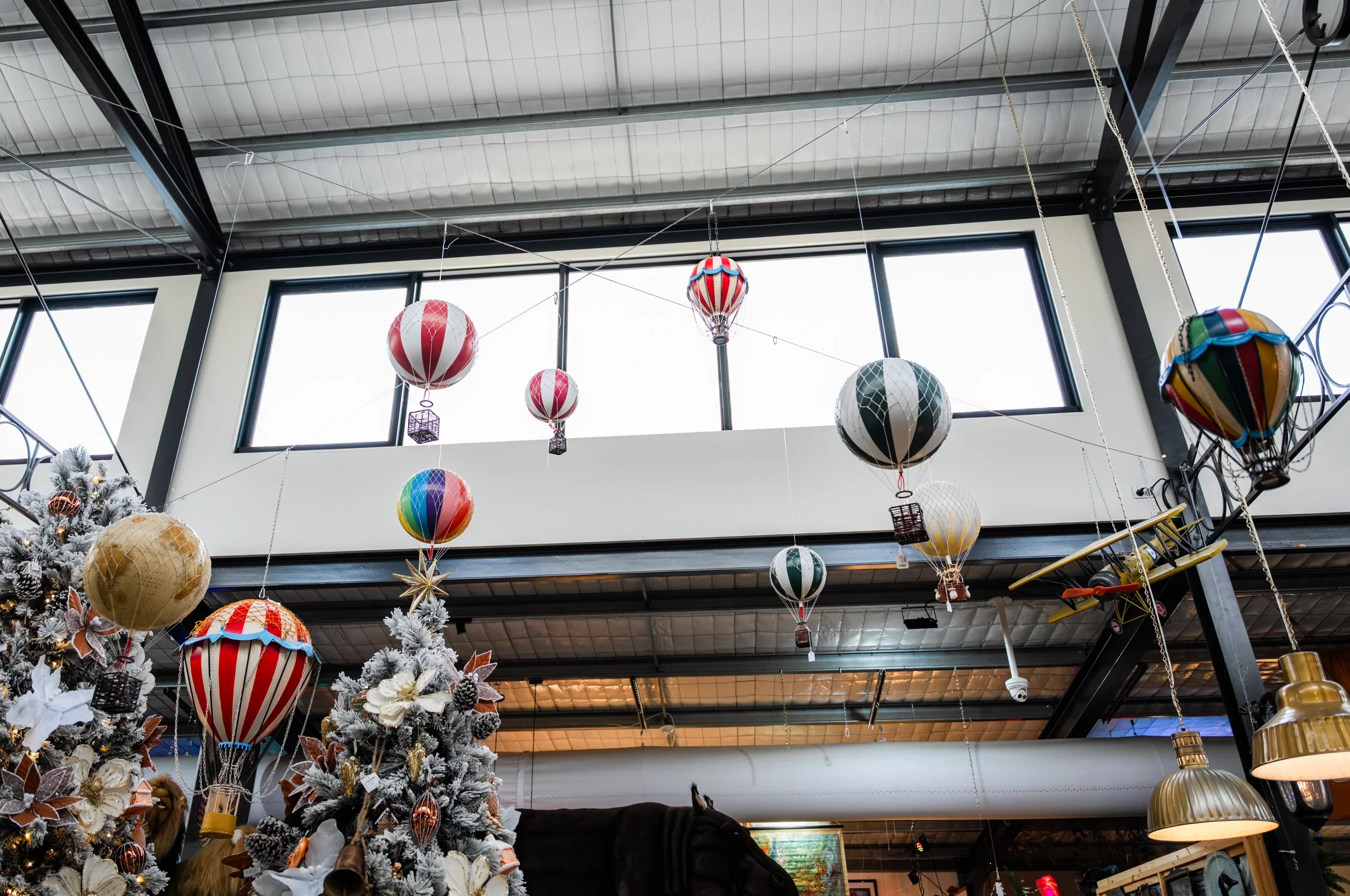 Indoor space decorated with hanging colorful hot air balloon ornaments and Christmas trees with ornaments.