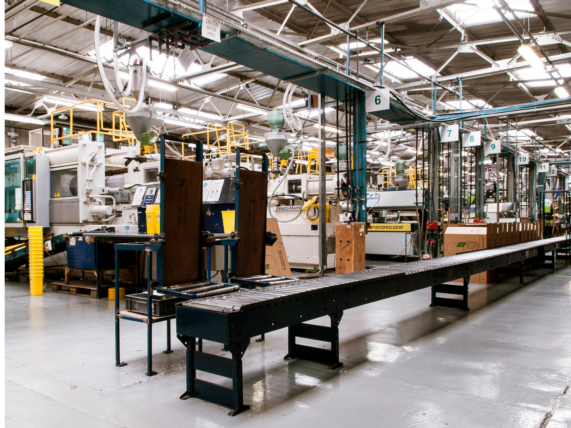 Une usine ou une chaîne de production avec plusieurs machines industrielles alignées, un tapis roulant, et un environnement éclairé par des lumières naturelles et électriques.