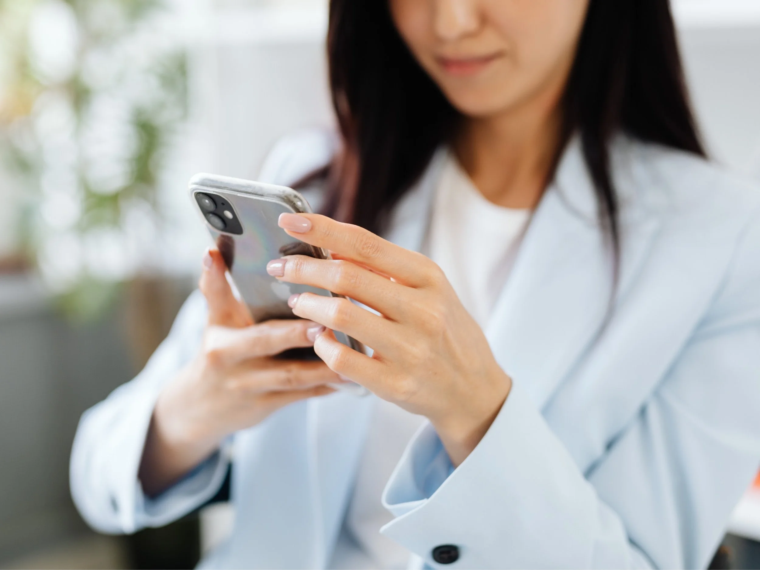 Une femme en blouse blanche utilisant un téléphone portable dans un environnement intérieur avec beaucoup de lumière naturelle.
