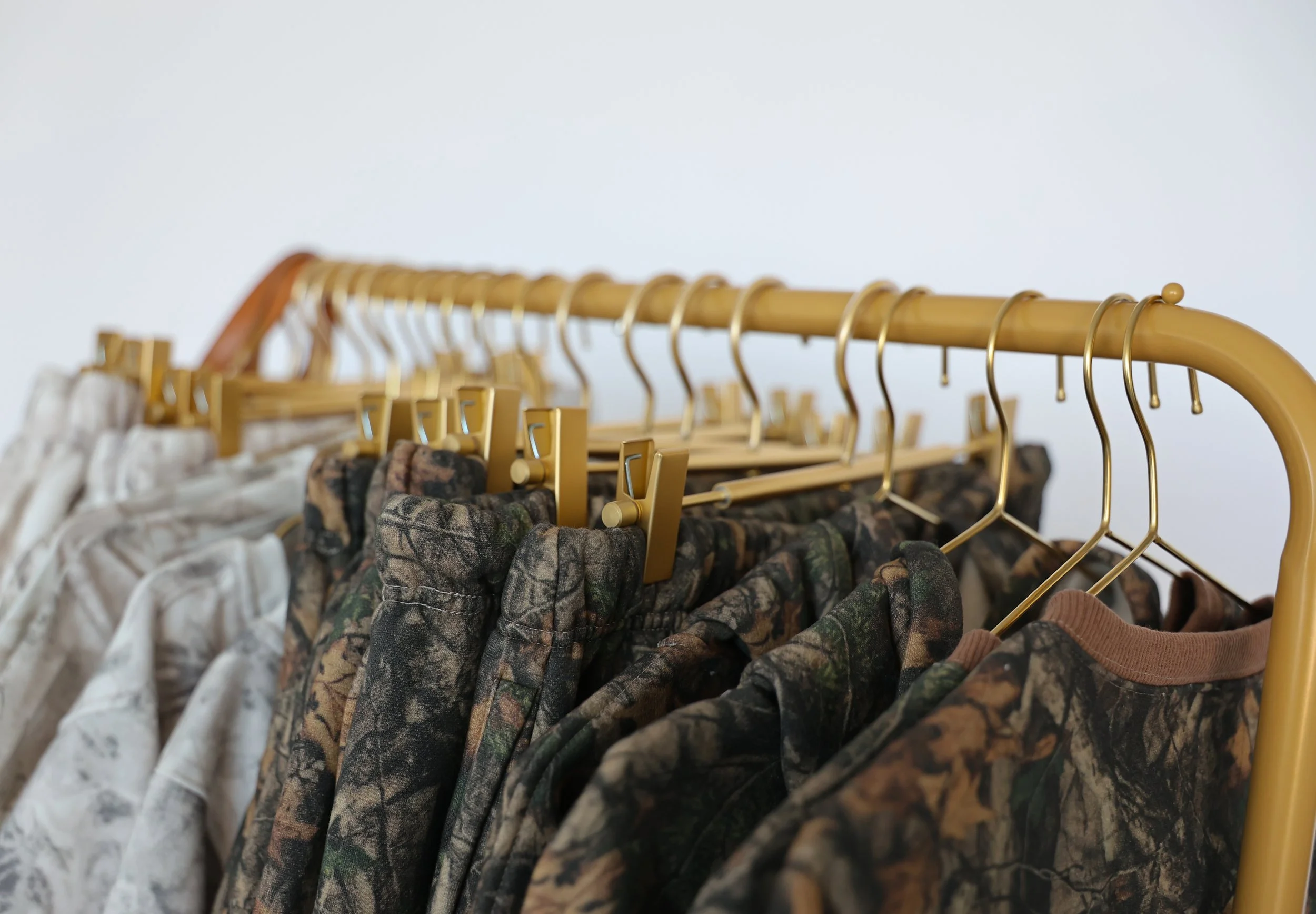 Clothing rack with camouflage and white patterned shirts hanging on gold hangers.
