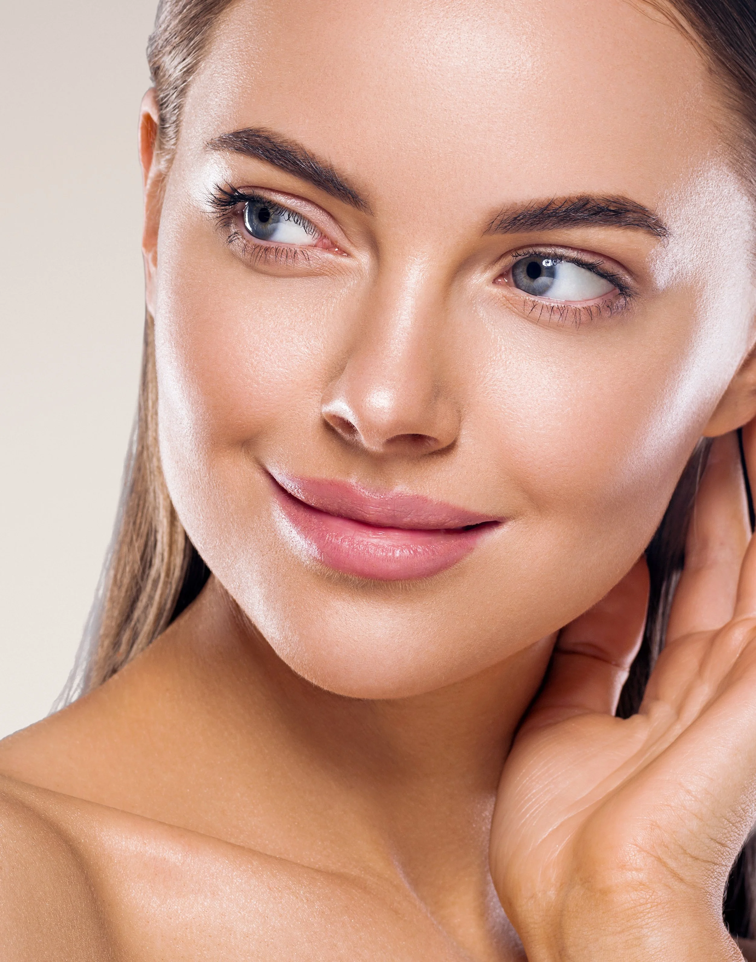 Close-up of a smiling woman with clear skin and blue eyes, gently touching her ear