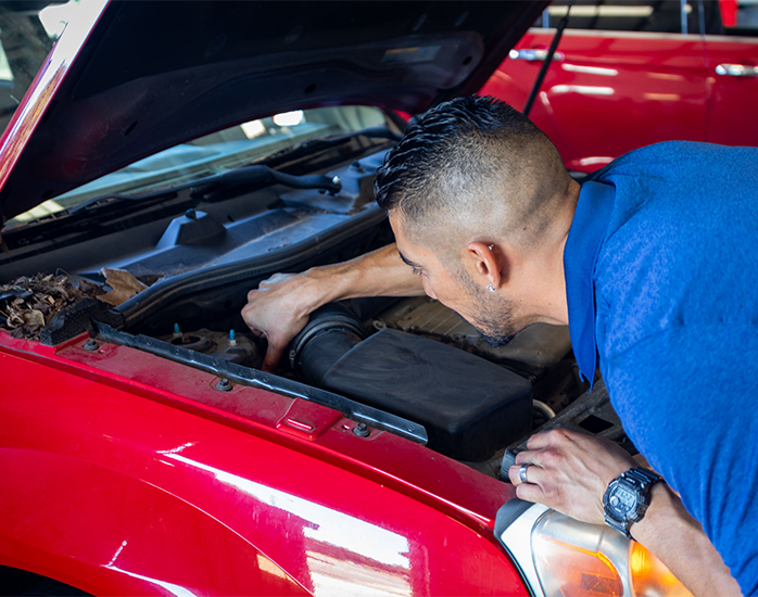 Mechanic inspecting the engine under the open hood of a red car at Rochas Auto Service in Redding and Anderson, California