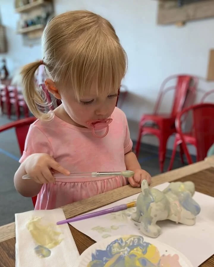 A child in pink paints a dog statue