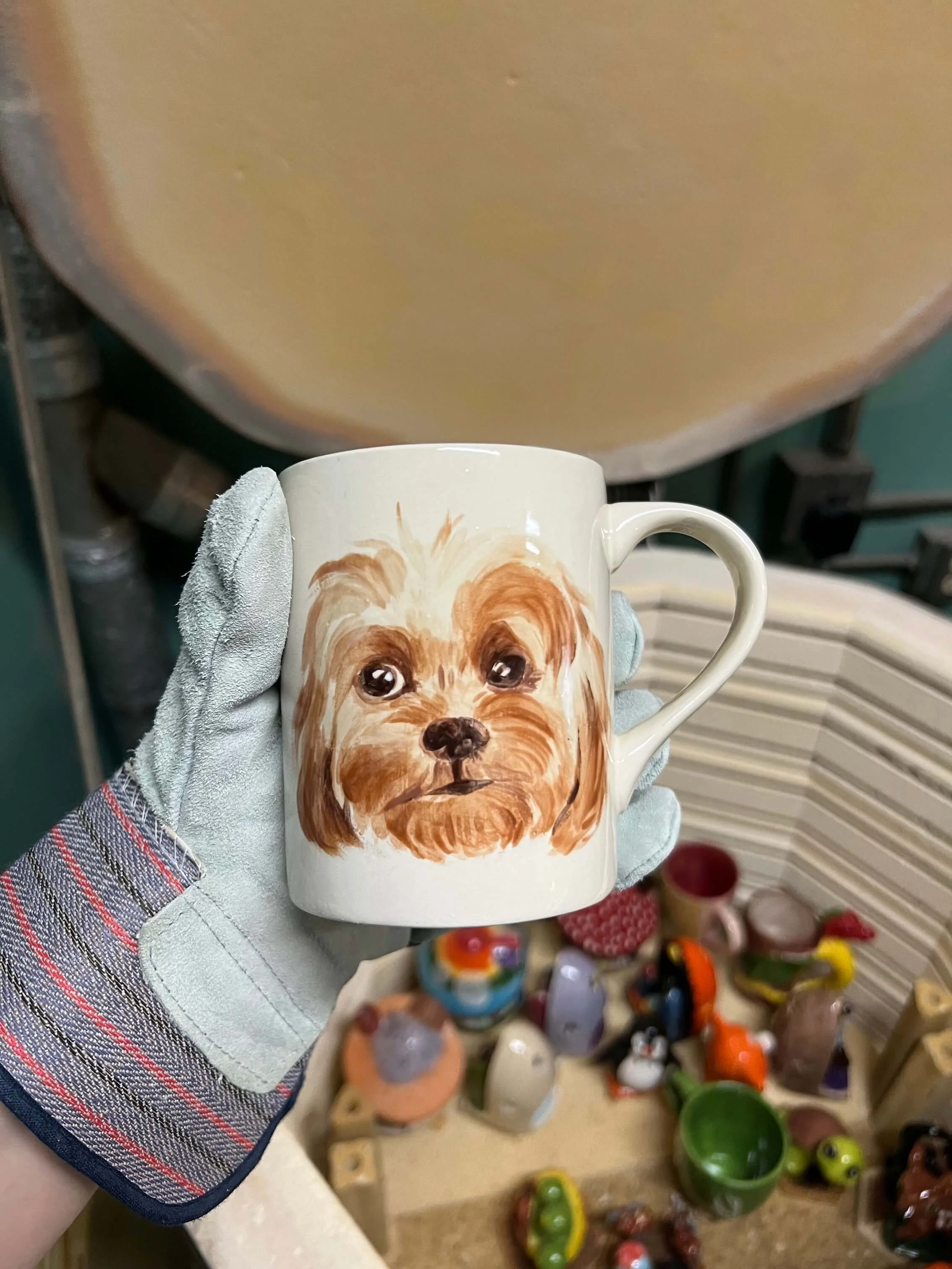 A gloved hand holds a dog mug over the kiln