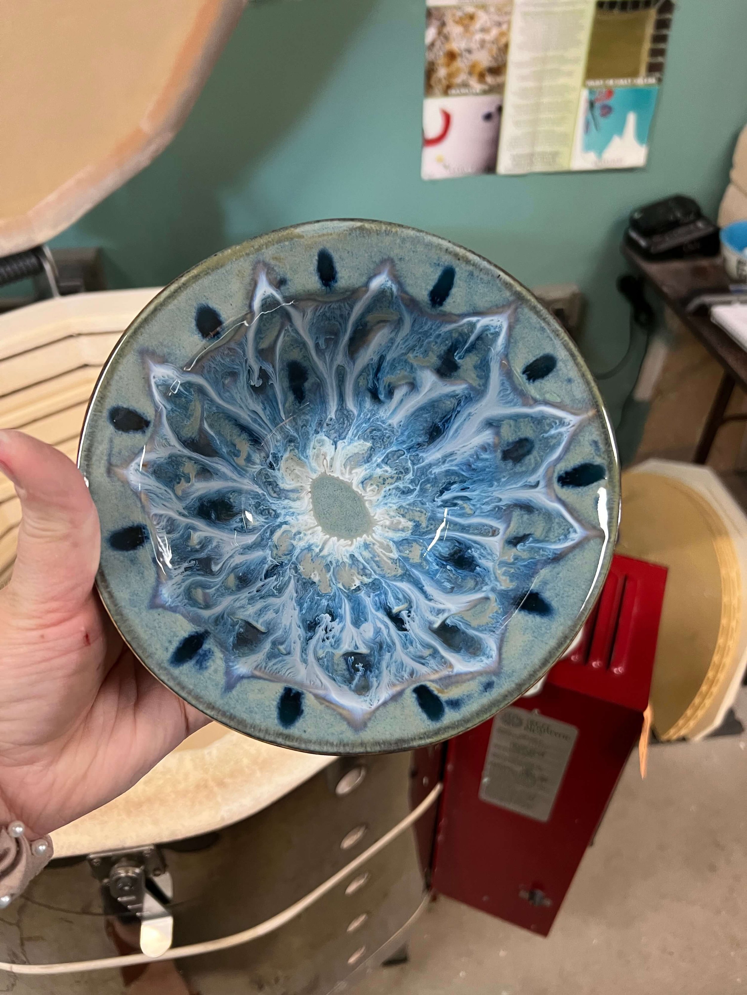 A hand holds blue stoneware above a kiln