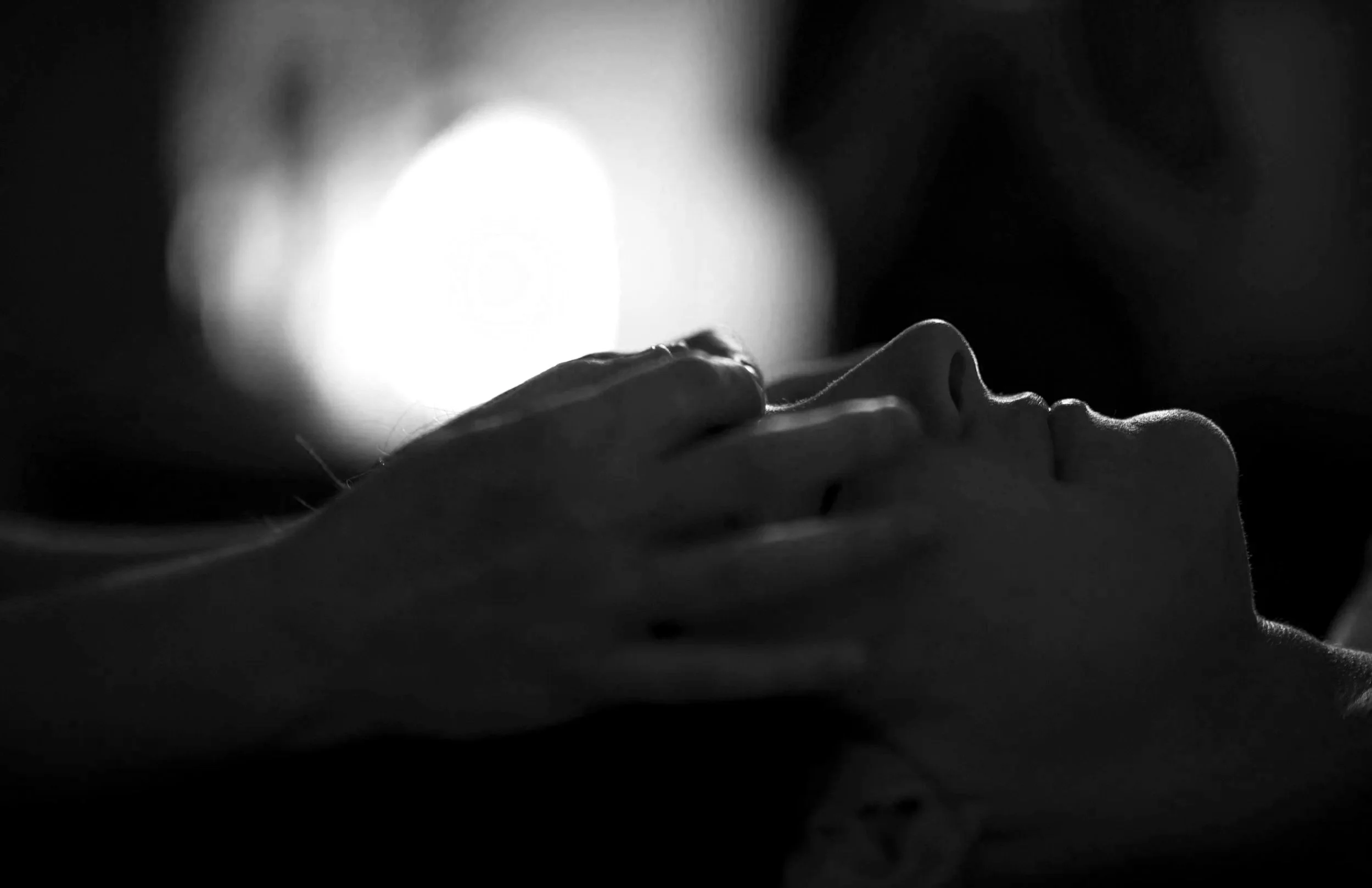 Black and white photo of a person's face in profile, eyes closed, with a hand gently touching their forehead.