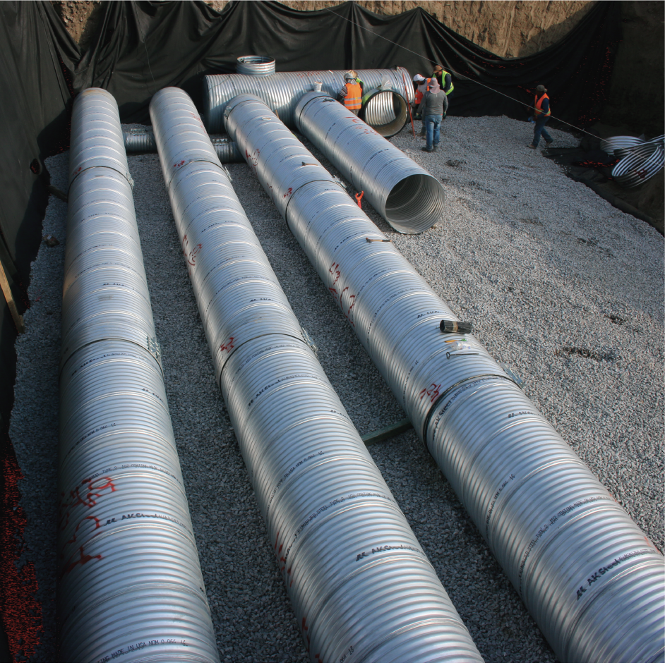 Tuberías de metal en una excavación, con trabajadores inspeccionando la obra.