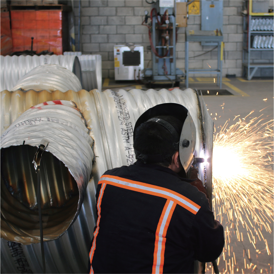Trabajador soldando una tubería grande en un taller industrial con chispas volando.