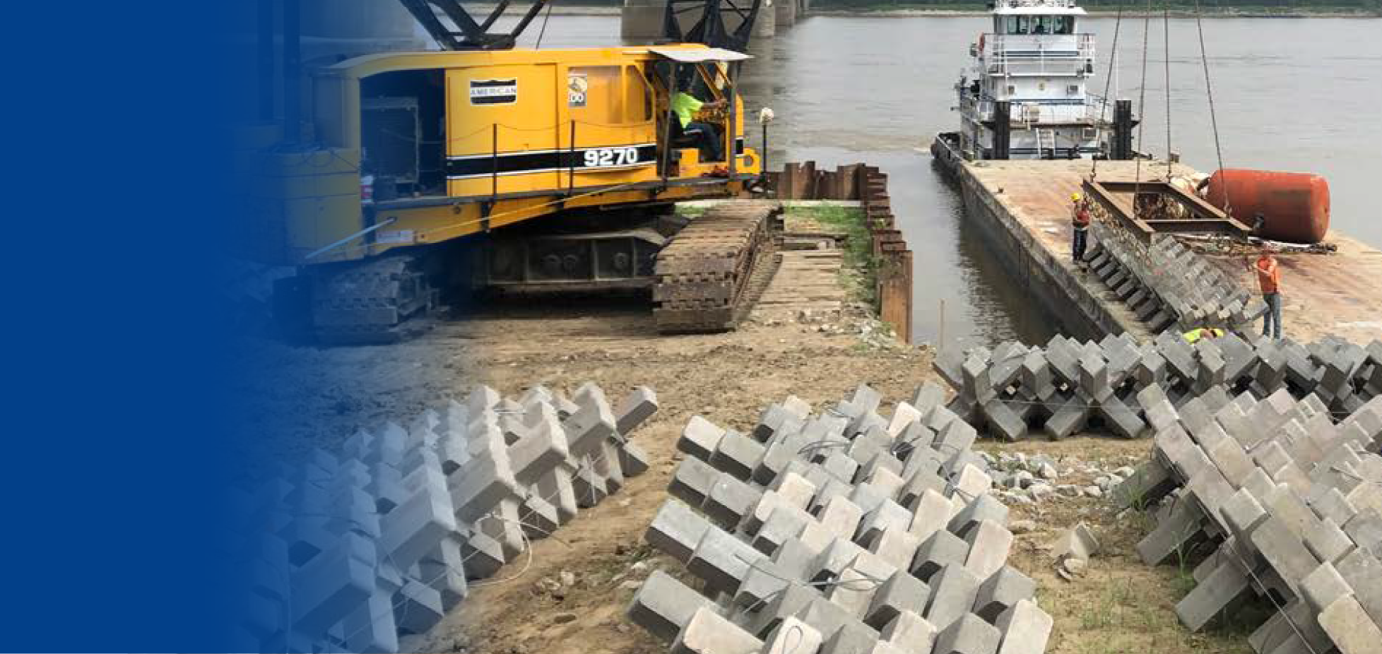 Trabajadores de construcción colocando bloques de concreto en un muelle junto a un río, con maquinaria pesada y barcos en el fondo.