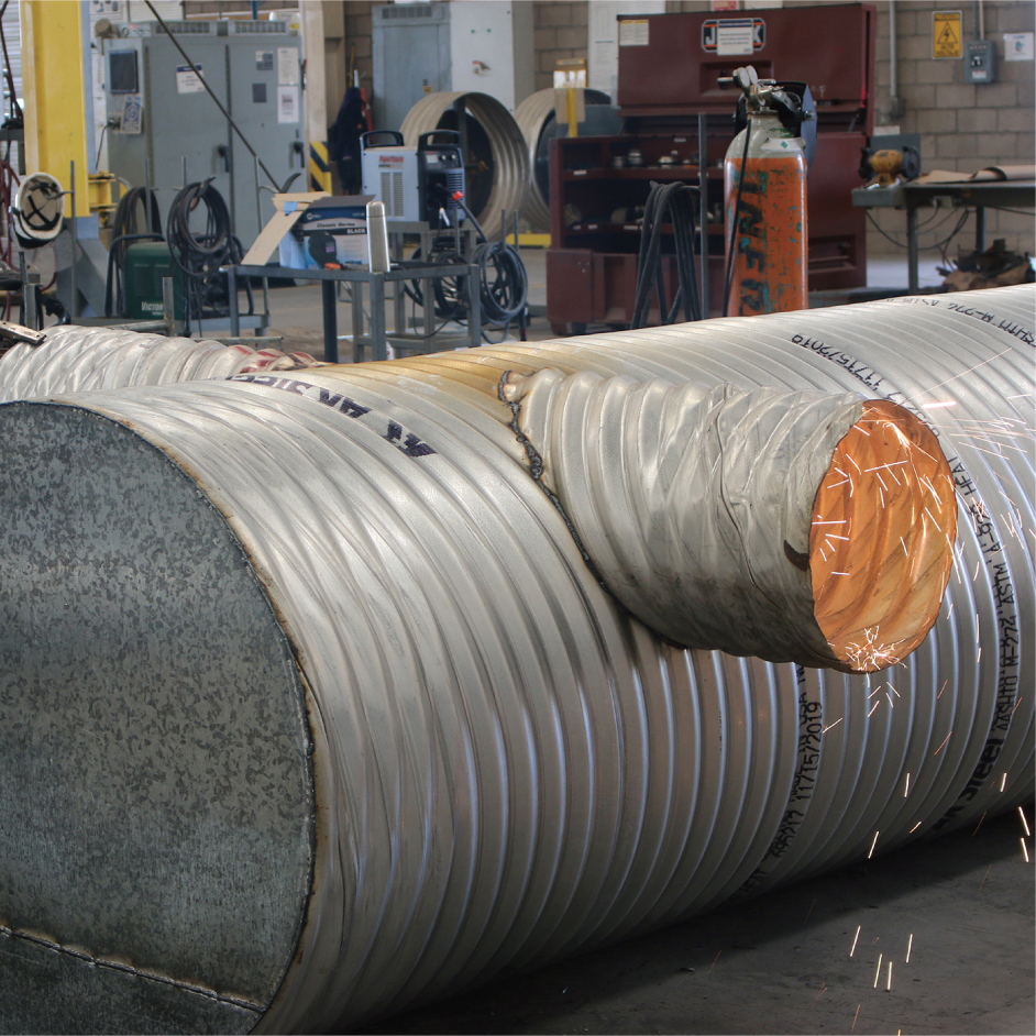 Tubo de gran tamaño en un taller industrial, con soldaduras y equipo de soldadura a su alrededor.