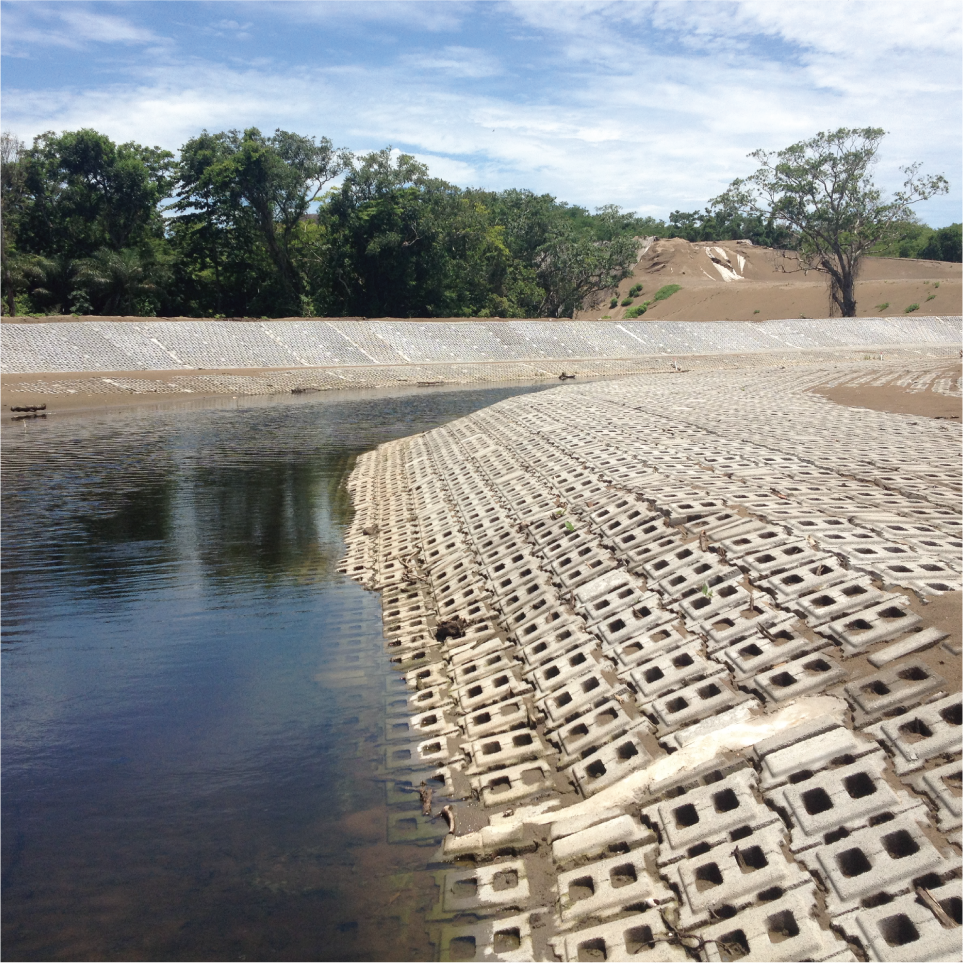 Represa con tapa de tapas de concreto cerca del agua, rodeada de árboles y tierra en un día soleado.