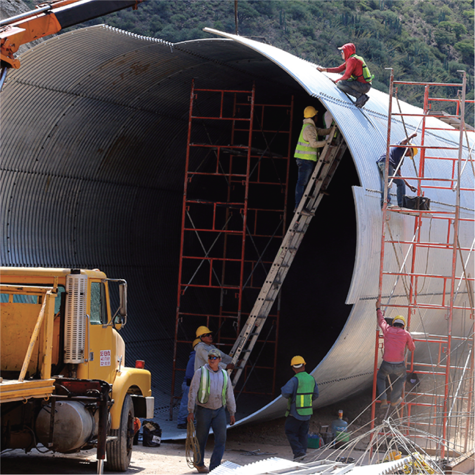 Trabajadores ensamblando una gran estructura metálica en un sitio de construcción rodeado de áreas verdes.