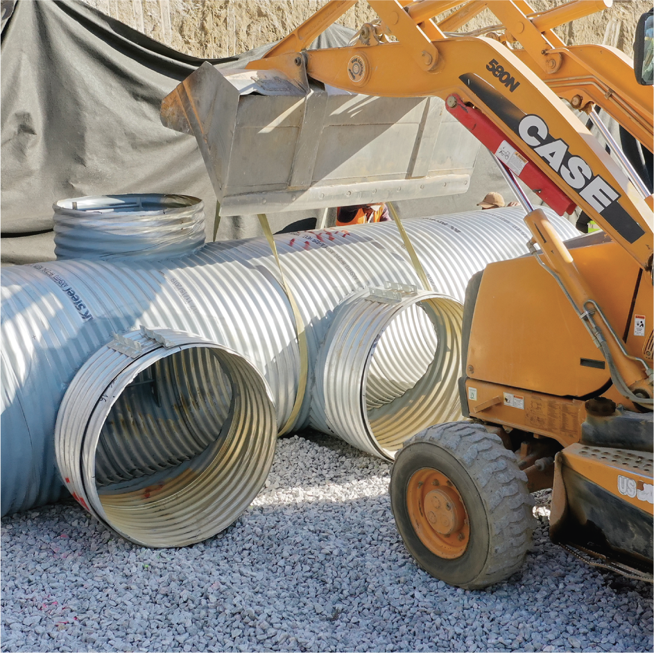 Excavadora operando en un sitio de construcción con tuberías de gran tamaño y grava en el suelo.