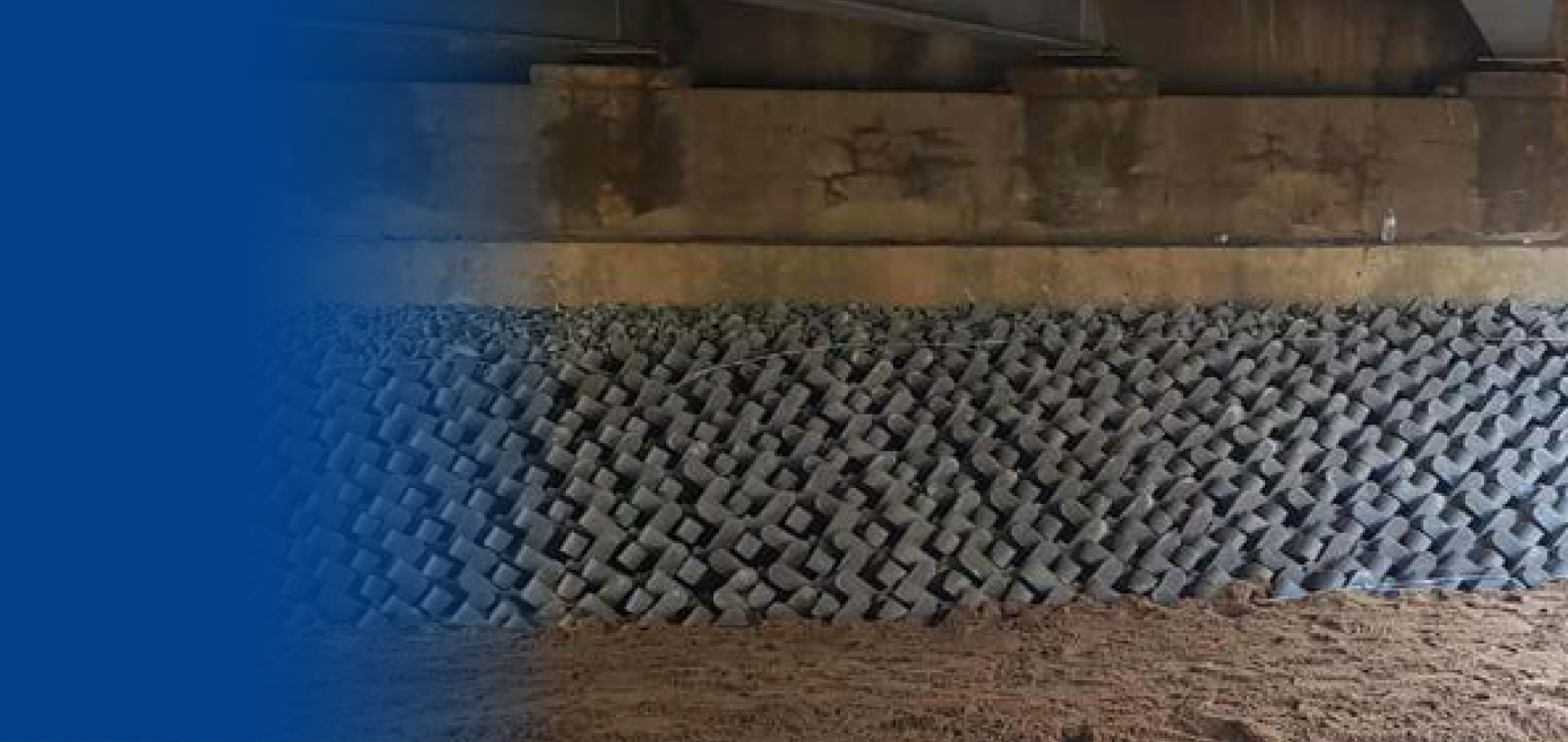 Muro de bloques de piedra en la base y concreto en la parte superior, con suelo de tierra delante.