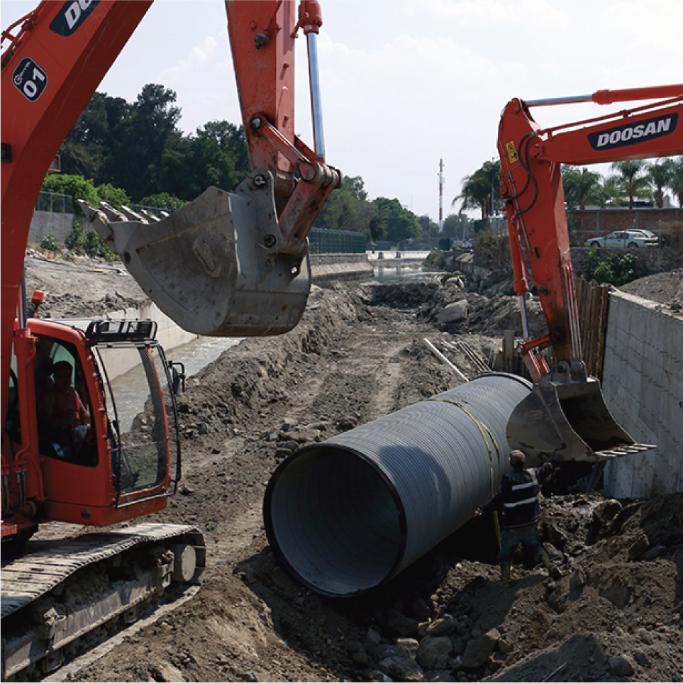 Maquinaria de construcción colocando una tubería grande en una excavación en tierra.
