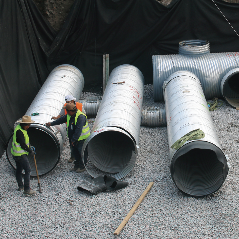 Tres trabajadores en un sitio de construcción ensamblando tuberías de metal grande sobre una base de grava.