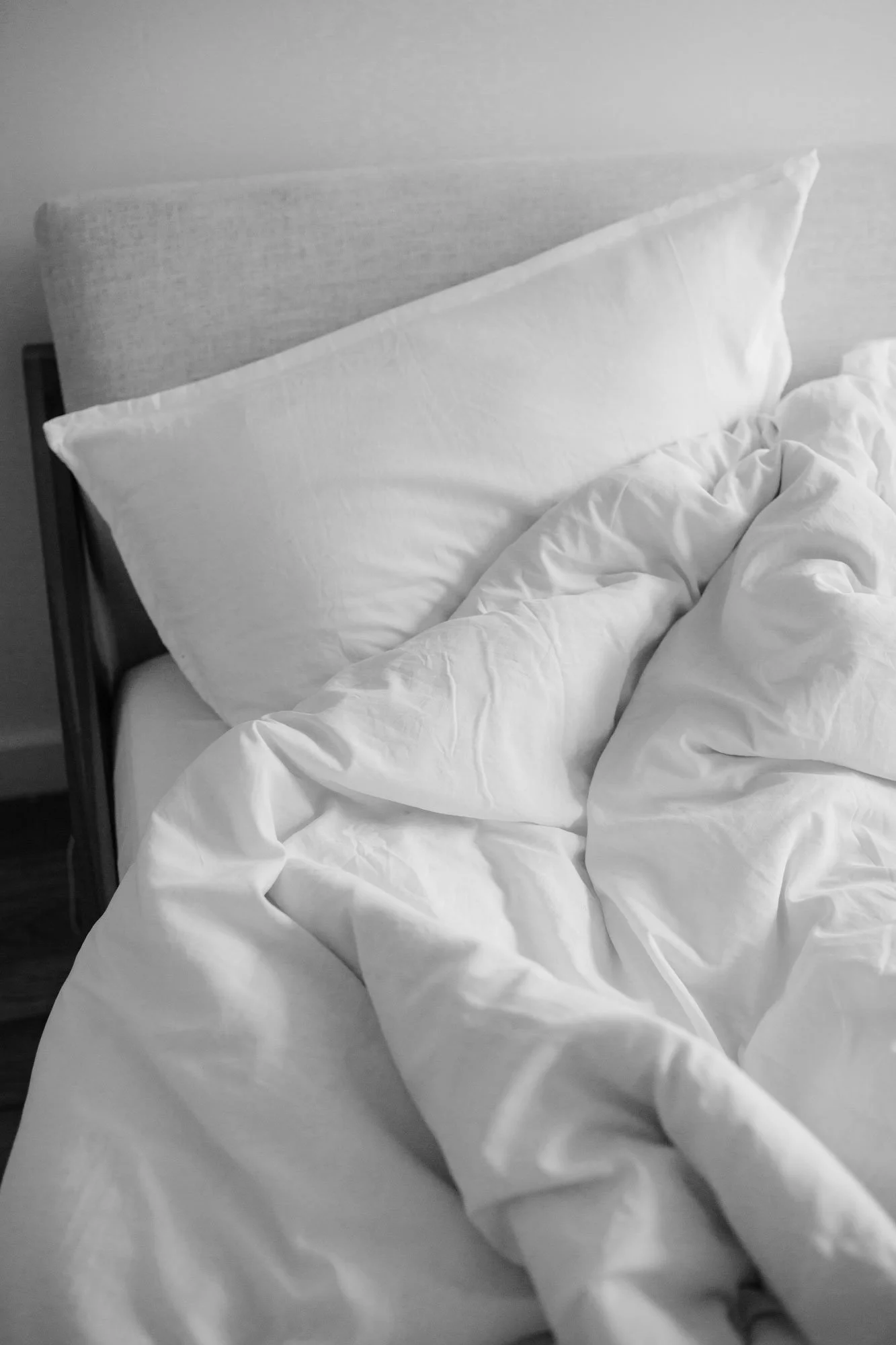 A bed with white sheets, pillowcases, and a headboard, all in black and white.